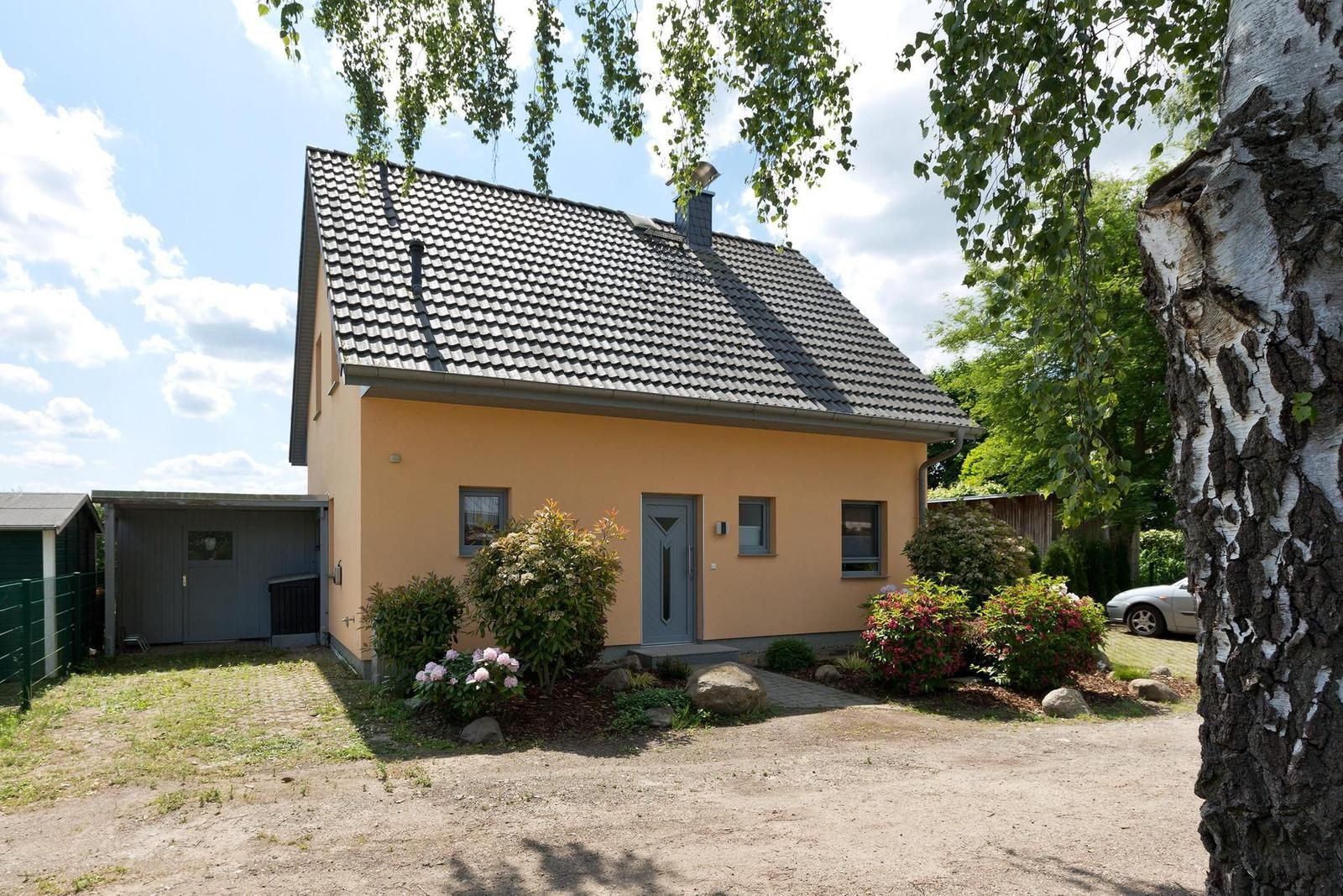 Ein gelbes Haus mit grauem Dach und blühenden Sträuchern im Vorgarten.