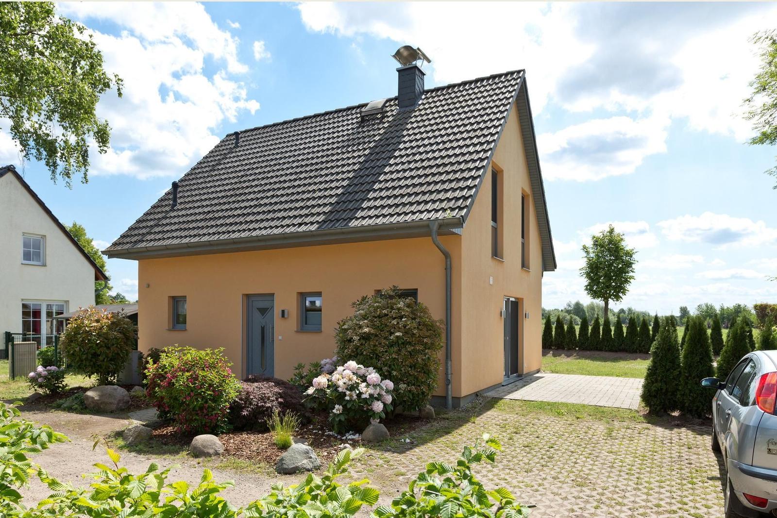 Ein gelbes Haus mit Dach und Garten. Ein Auto steht auf dem Hof.