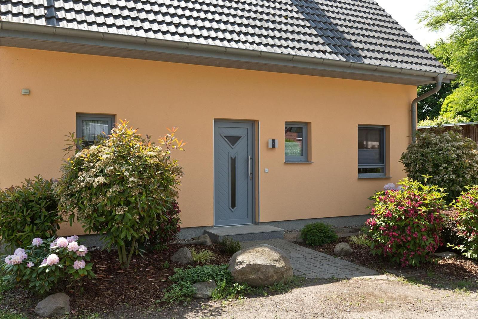 Ein Haus mit gelber Fassade, grauer Tür und einem gepflasterten Weg durch den Garten.