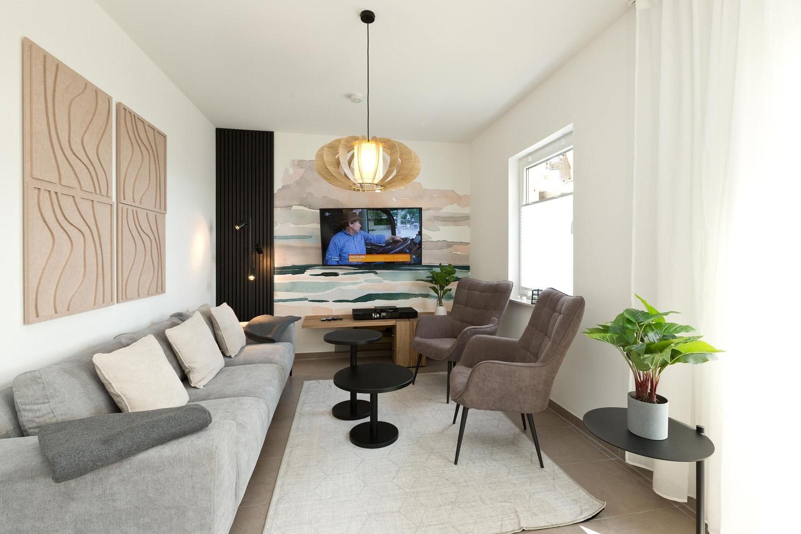 Wohnzimmer mit Sofa, zwei Sesseln, Fernseher und Pflanzen.