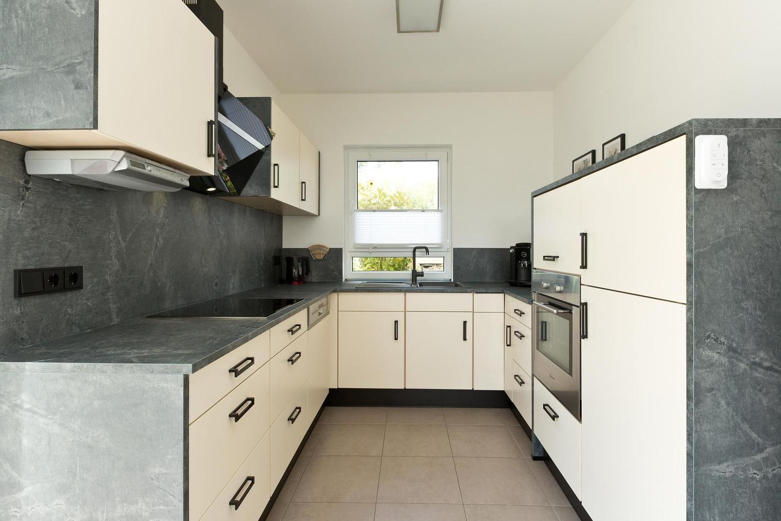 Küche mit weißen Schränken, dunklem Arbeitsplatz und Fenster