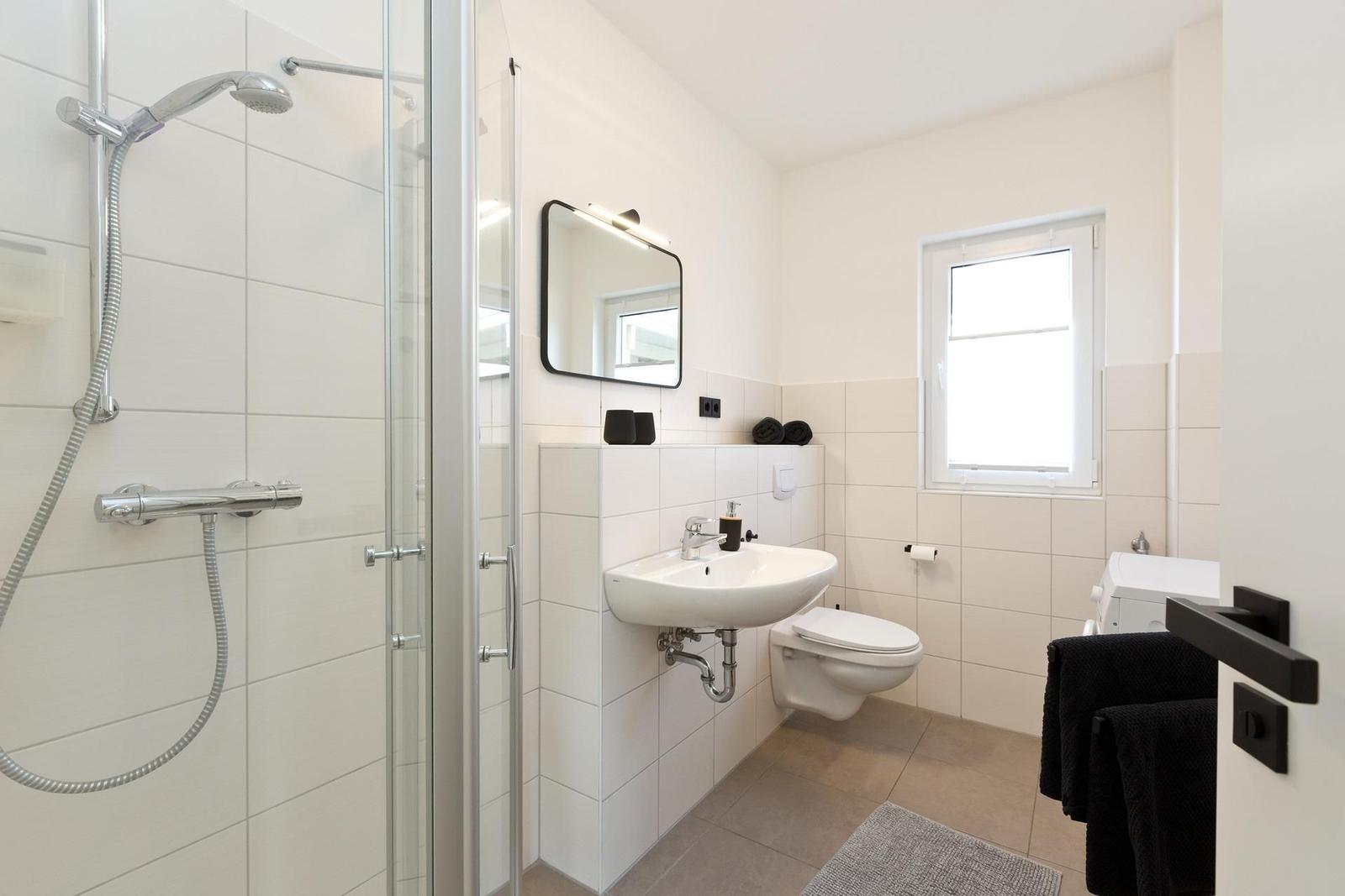 Badezimmer mit Dusche, Waschbecken und WC. Fenster sorgt für Tageslicht.