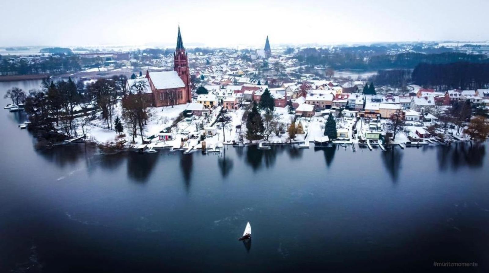 Schneebedeckte Stadt mit Kirche und Boot auf ruhigem Wasser.