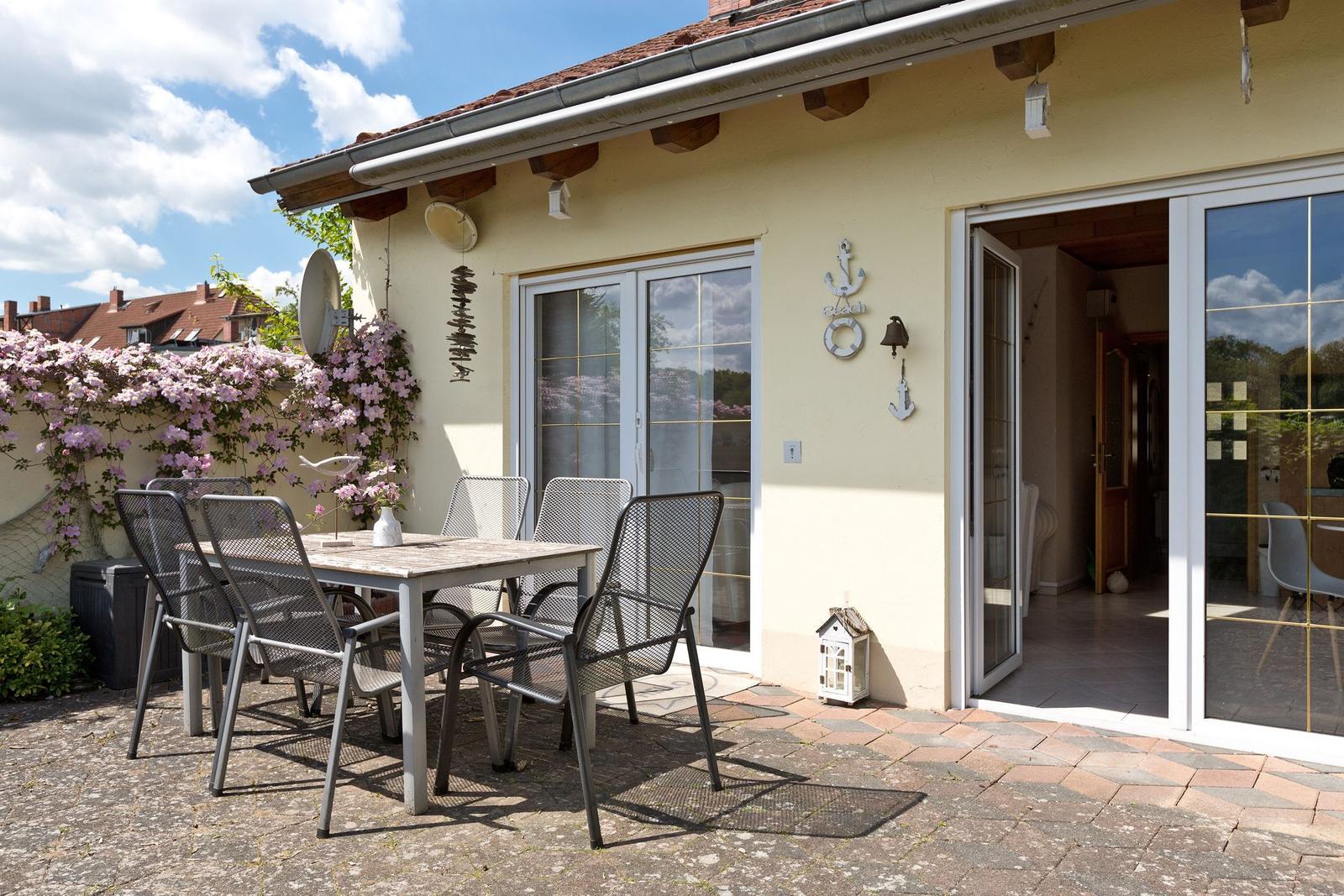 Terrasse mit Tisch und Stühlen, Blick in das Haus, Blumen an der Wand.
