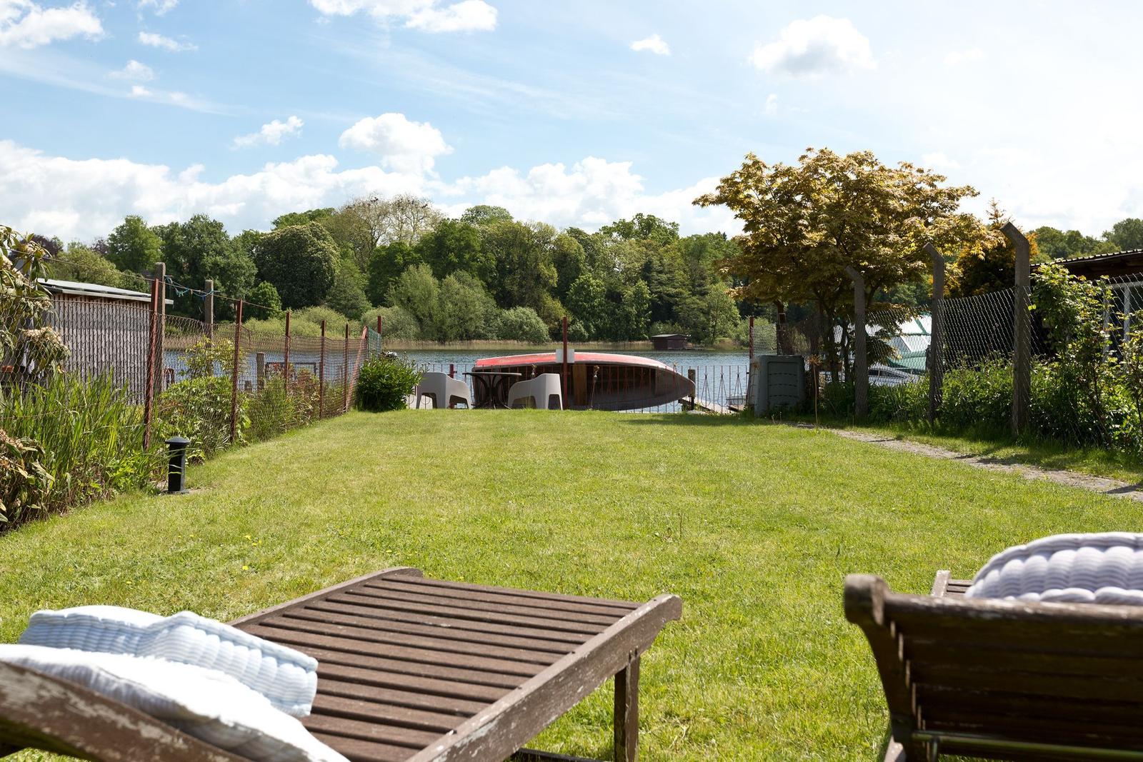 Garten mit Liegestühlen und Blick auf einen See mit Boot.
