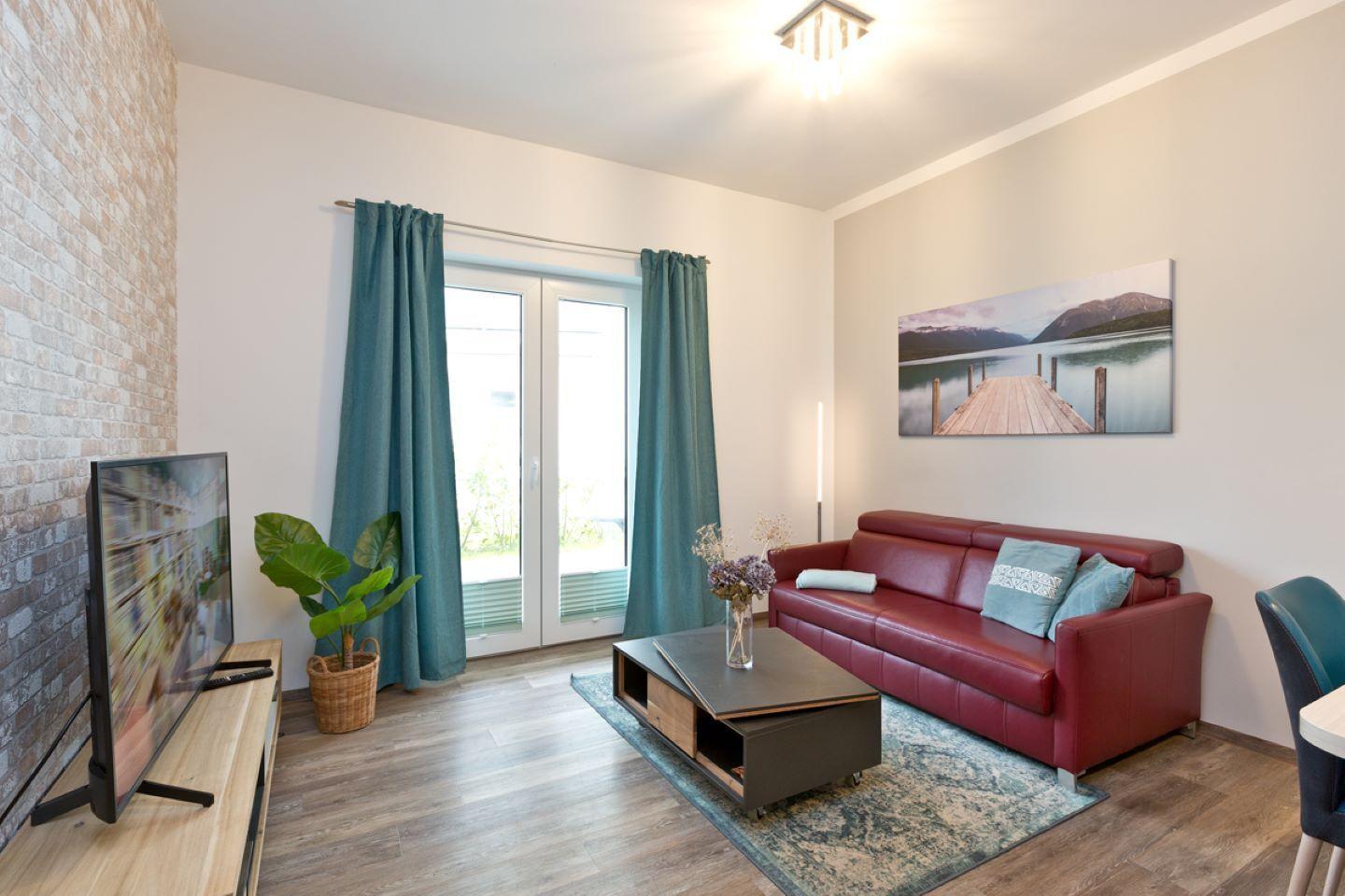 Wohnzimmer mit rotem Sofa, Fernseher und Fenster mit grünen Vorhängen.
