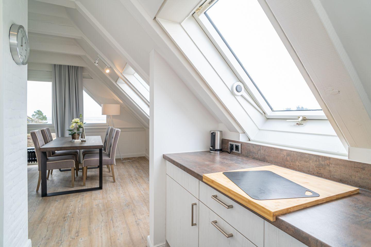 Kitchen with worktop and dining area under sloped ceilings with windows.