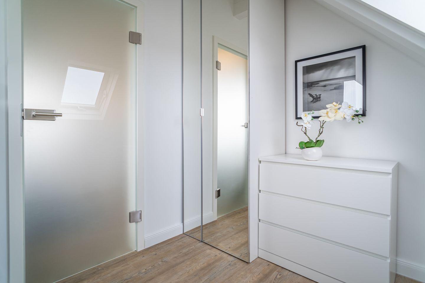 A room with a white dresser, mirror, and glass door. A white orchid sits on the dresser.