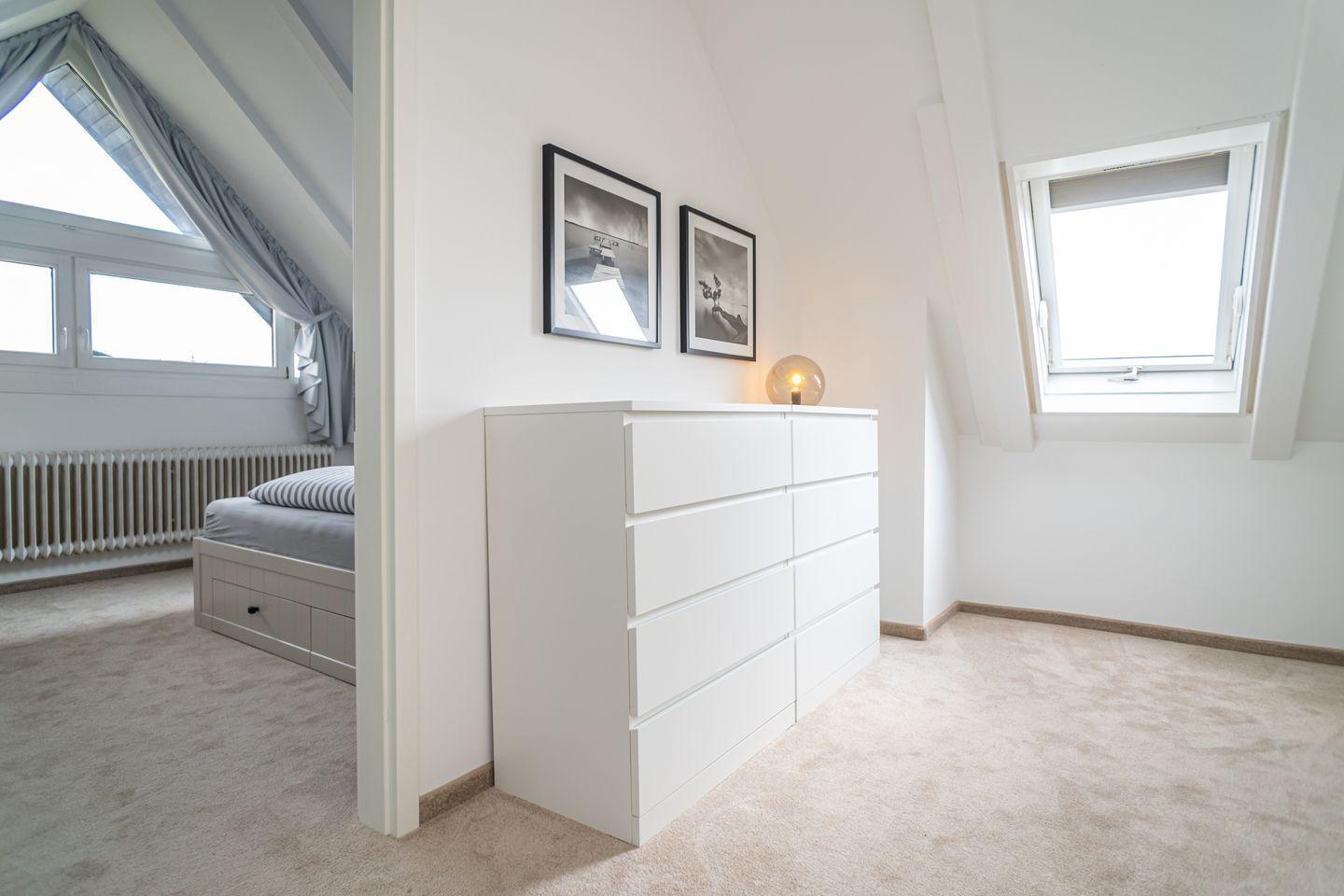 Bedroom with sloped ceiling, white dresser, and windows.