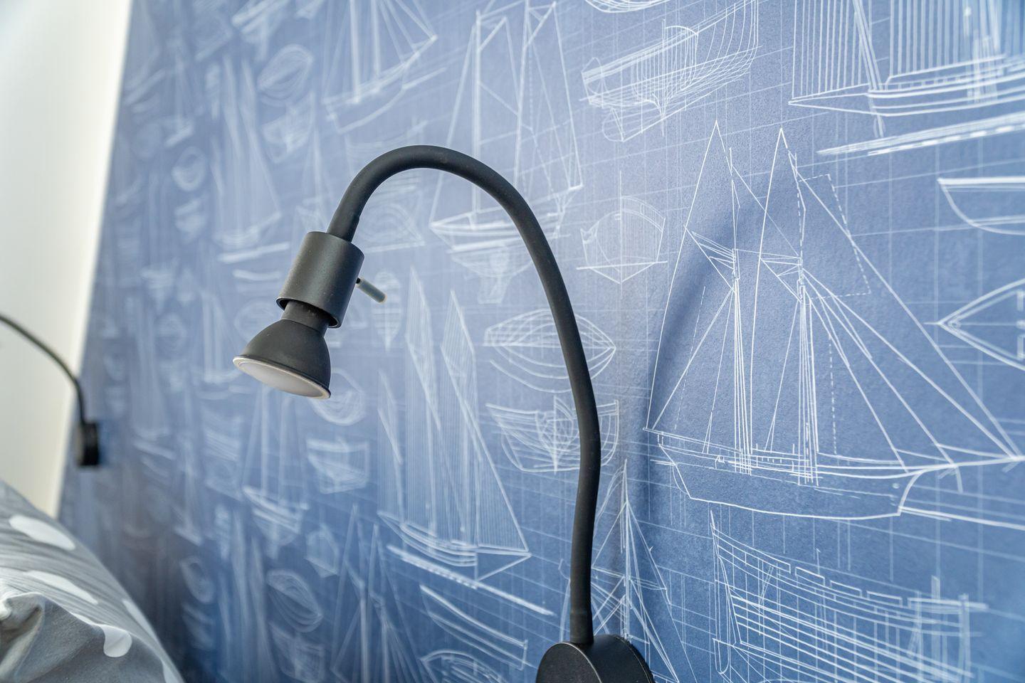Desk lamp in front of blue wallpaper with ship blueprints