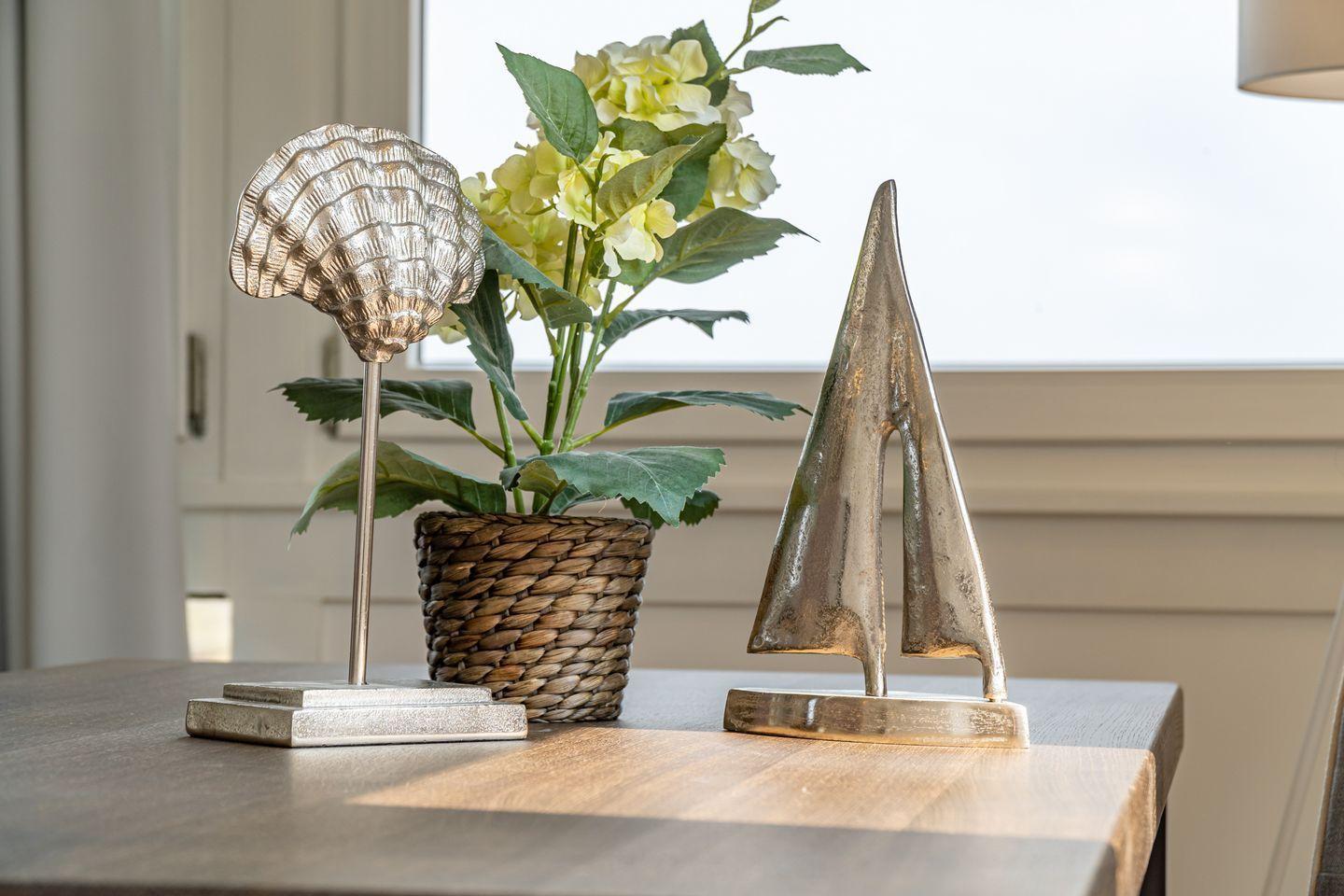Wooden table with decorative items: seashell, sailboat, and flower pot.
