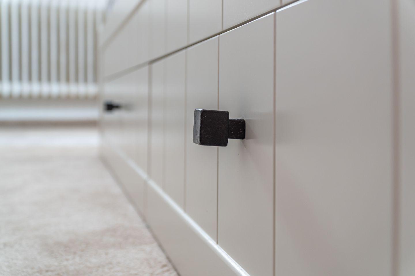 Black handle on a white cabinet with vertical panels.