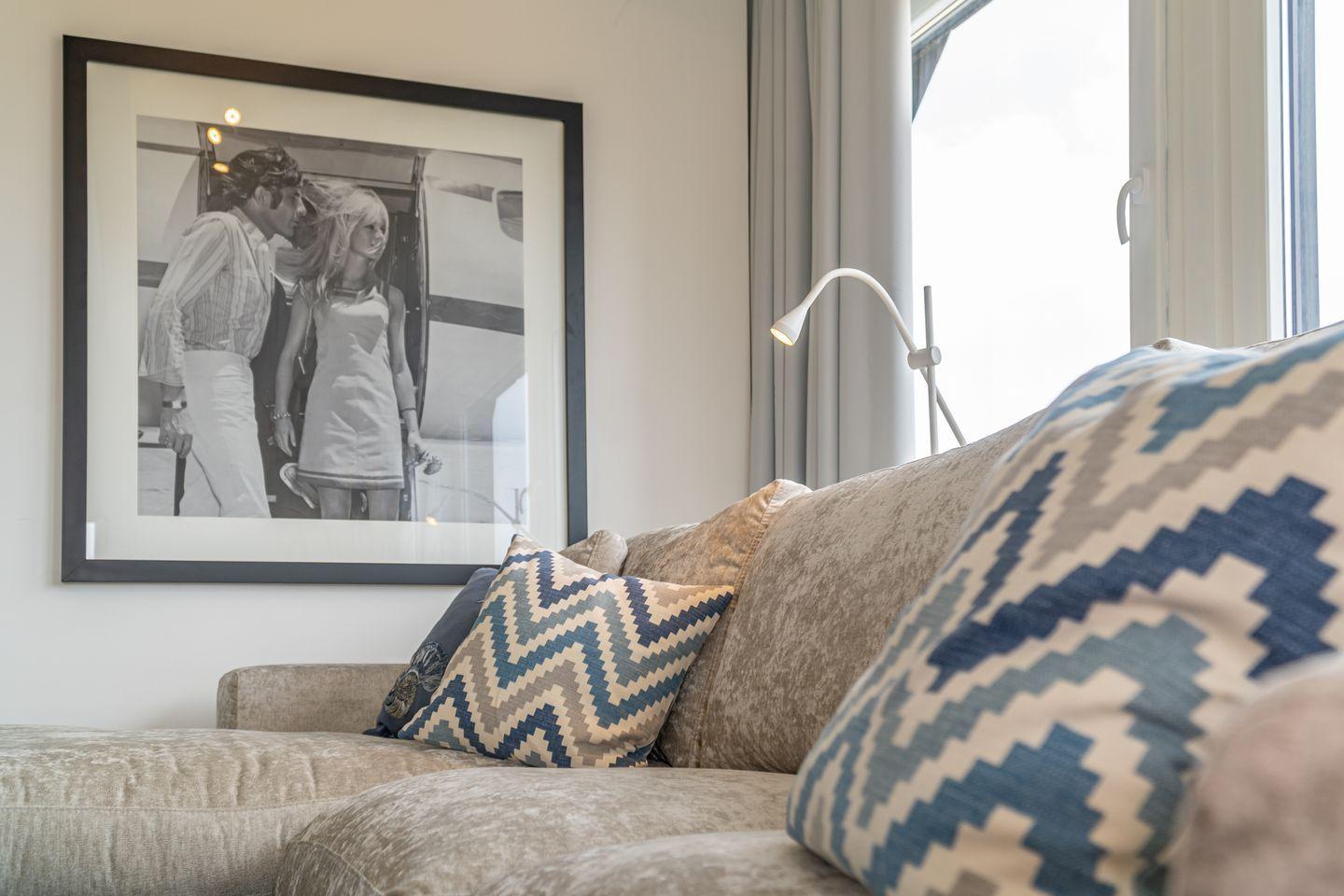 A sofa with cushions near a window and a picture on the wall.