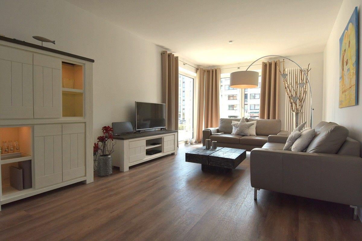 Wohnzimmer mit Sofa, Couchtisch und Fernseher. Holzboden und große Fenster.