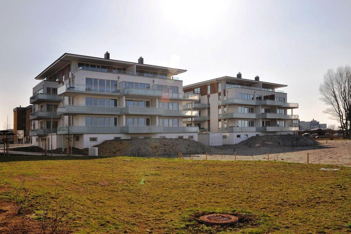 Moderne Mehrfamilienhaus mit Balkonen und Glasfronten. Grünfläche im Vordergrund.