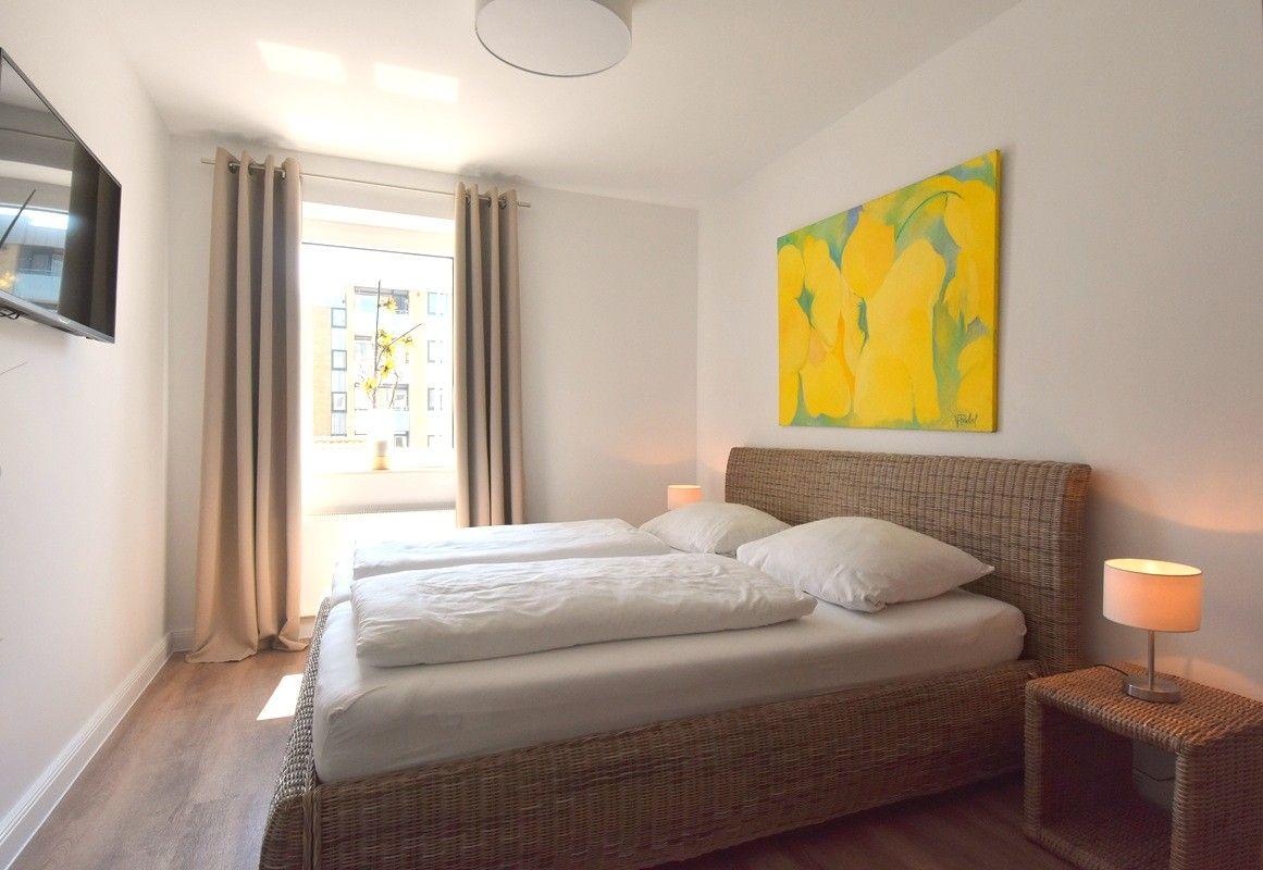 Schlafzimmer mit Doppelbett, Wandbild und Fenster. Holzfußboden und Nachttisch.