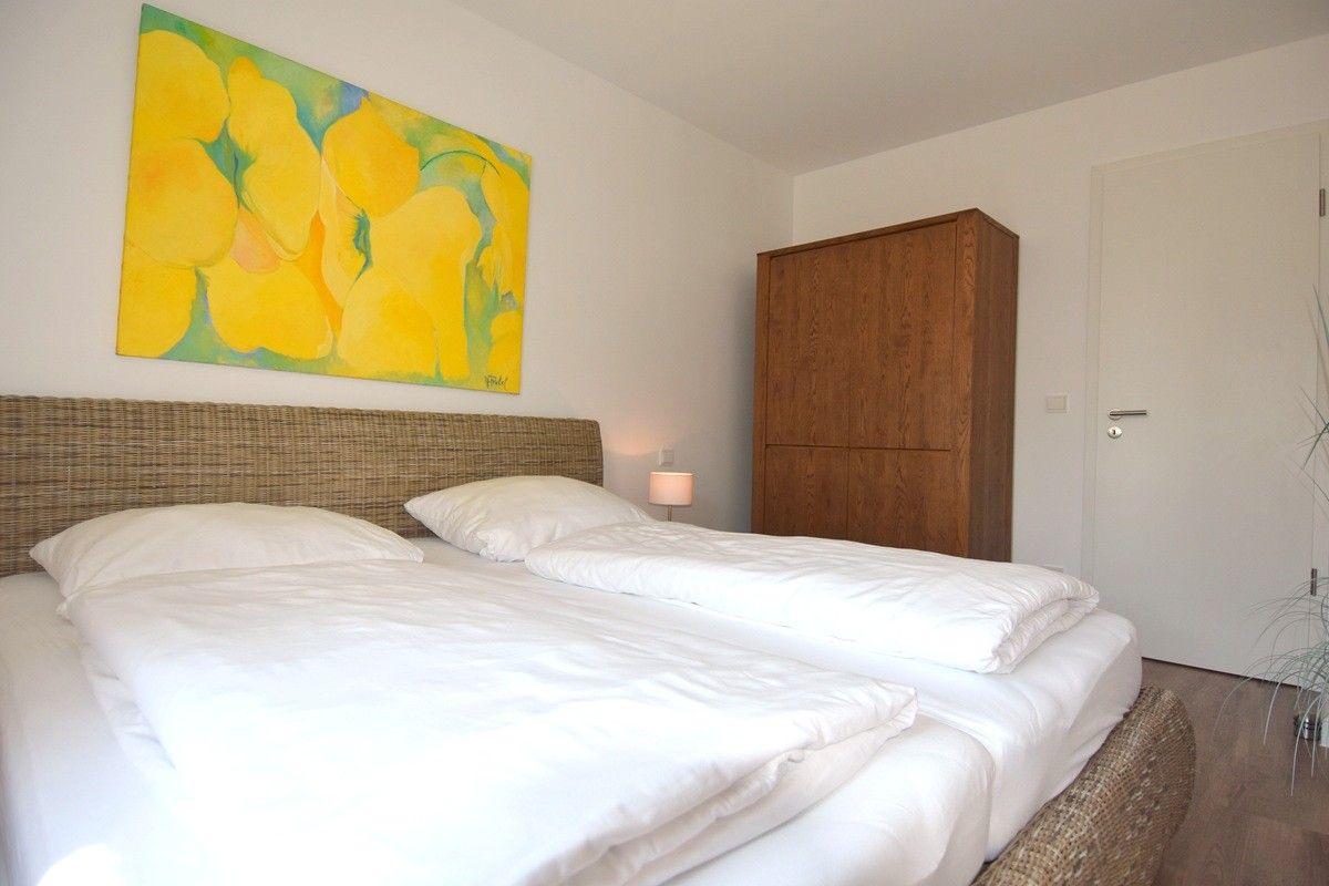 Schlafzimmer mit Doppelbett, Holzschrank und Wandbild mit gelben Blumen.