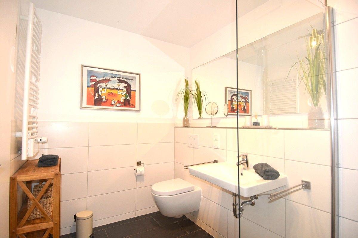 Badezimmer mit Dusche, Waschbecken und Toilette. Wandbild und Pflanzen sichtbar.