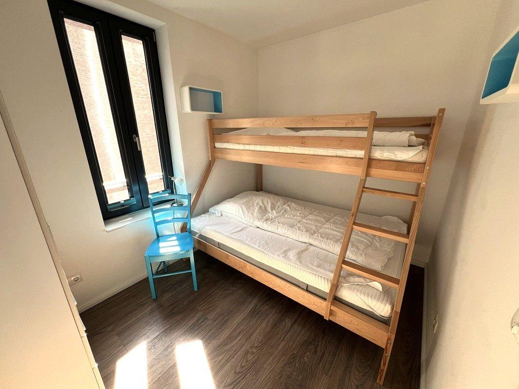 Zimmer mit Doppelstockbett, blauer Stuhl und Fenster mit Blick auf Außenbereich.