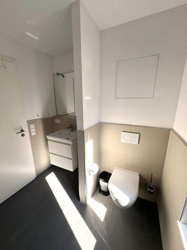 Badezimmer mit Toilette, Waschbecken und Spiegel. Fliesenboden und Wandverkleidung.