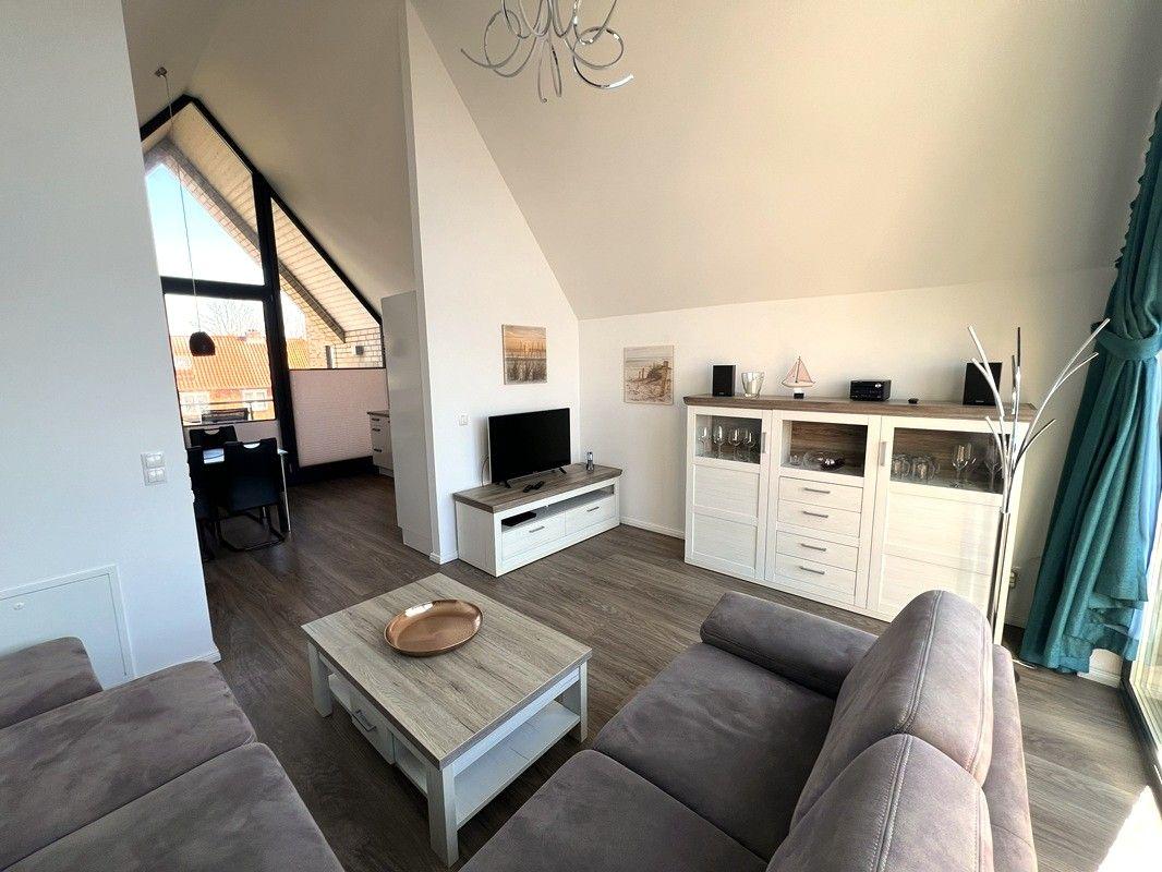 Wohnzimmer mit Sofa, Couchtisch und Fernseher. Blick in die Küche und auf die Terrasse.