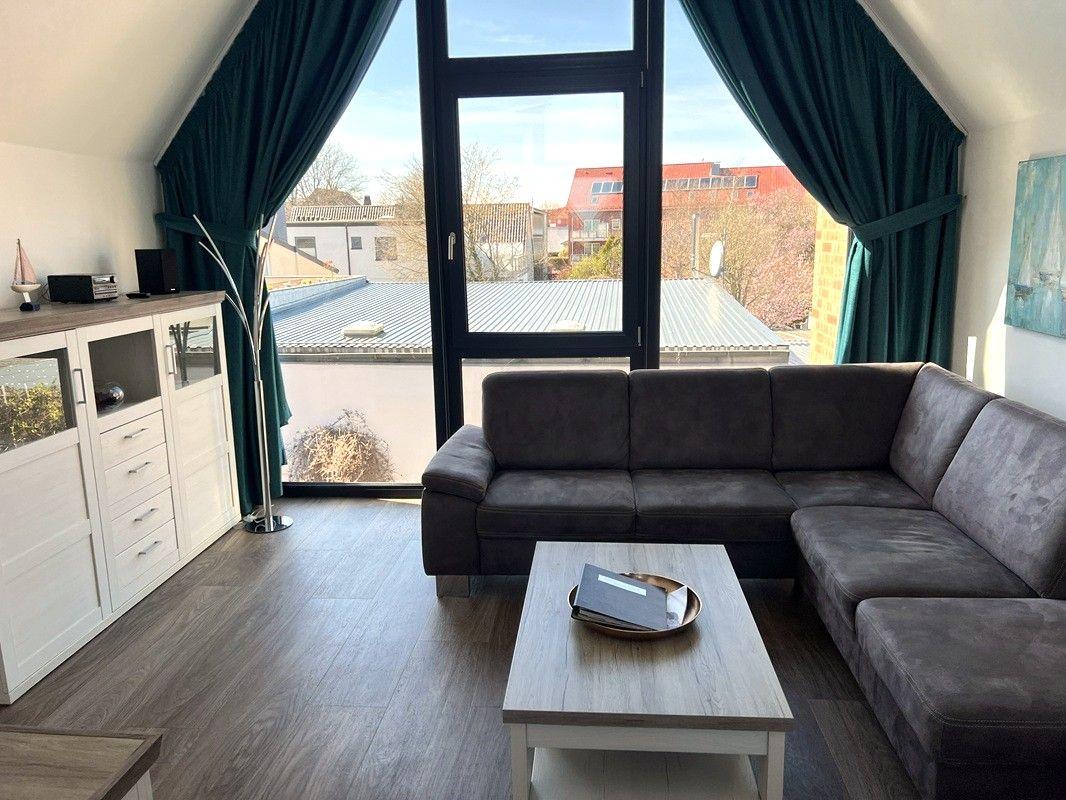 Wohnzimmer mit Sofa, Tisch und Fenster mit Blick auf Dächer.
