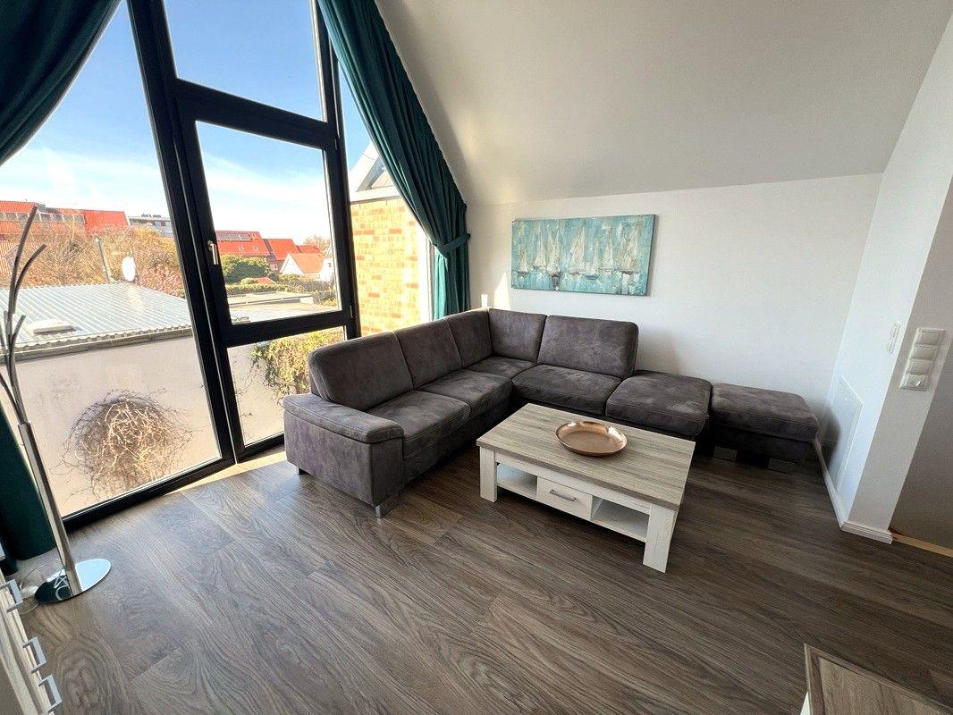 Wohnzimmer mit Ecksofa, Holzboden und großem Fenster mit Blick auf die Umgebung.