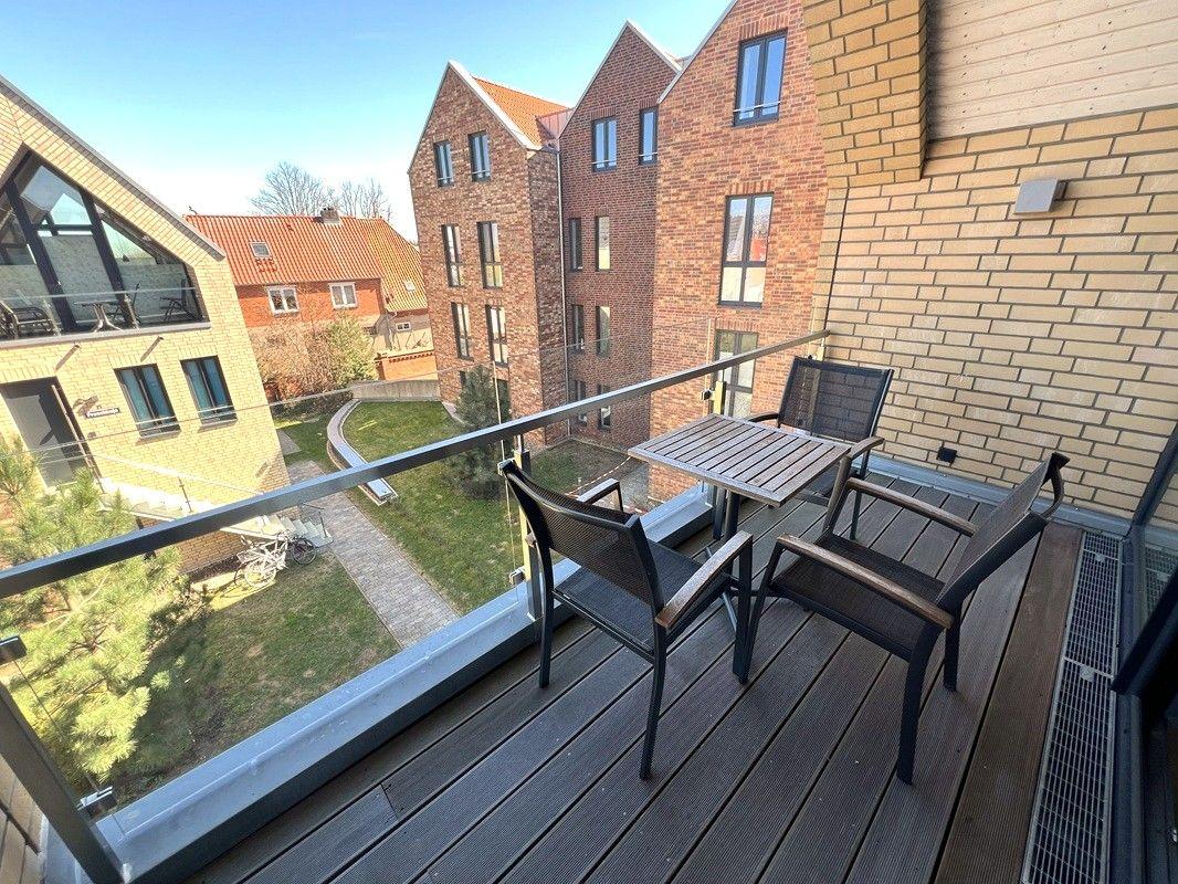 Terrasse mit Tisch und Stühlen, Blick auf Wohnhäuser und Grünfläche.