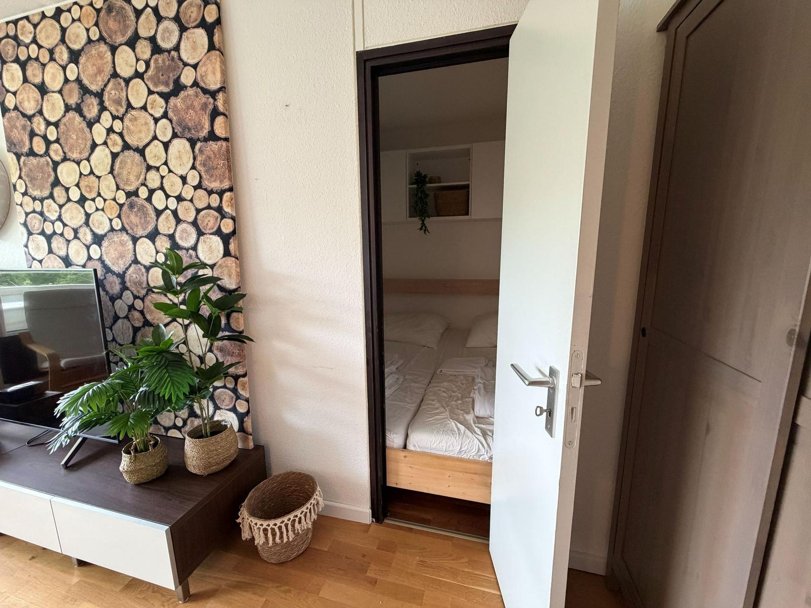 Ein Raum mit Holzfußboden, einer Tür zum Schlafzimmer und einer Wand mit Holzschliff-Motiv.