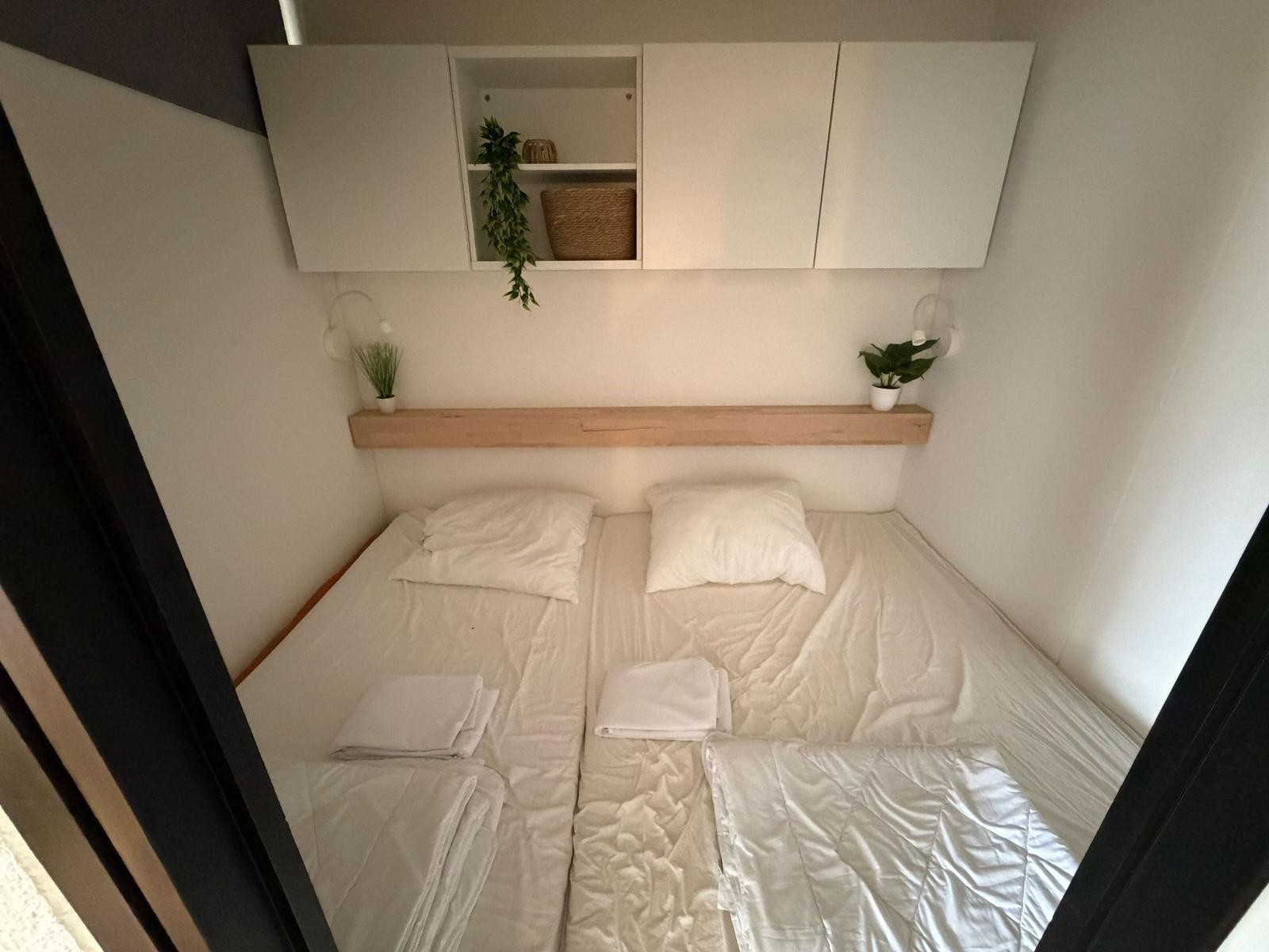 Schlafzimmer mit Bett, weißen Laken und Wandregalen mit Pflanzen.