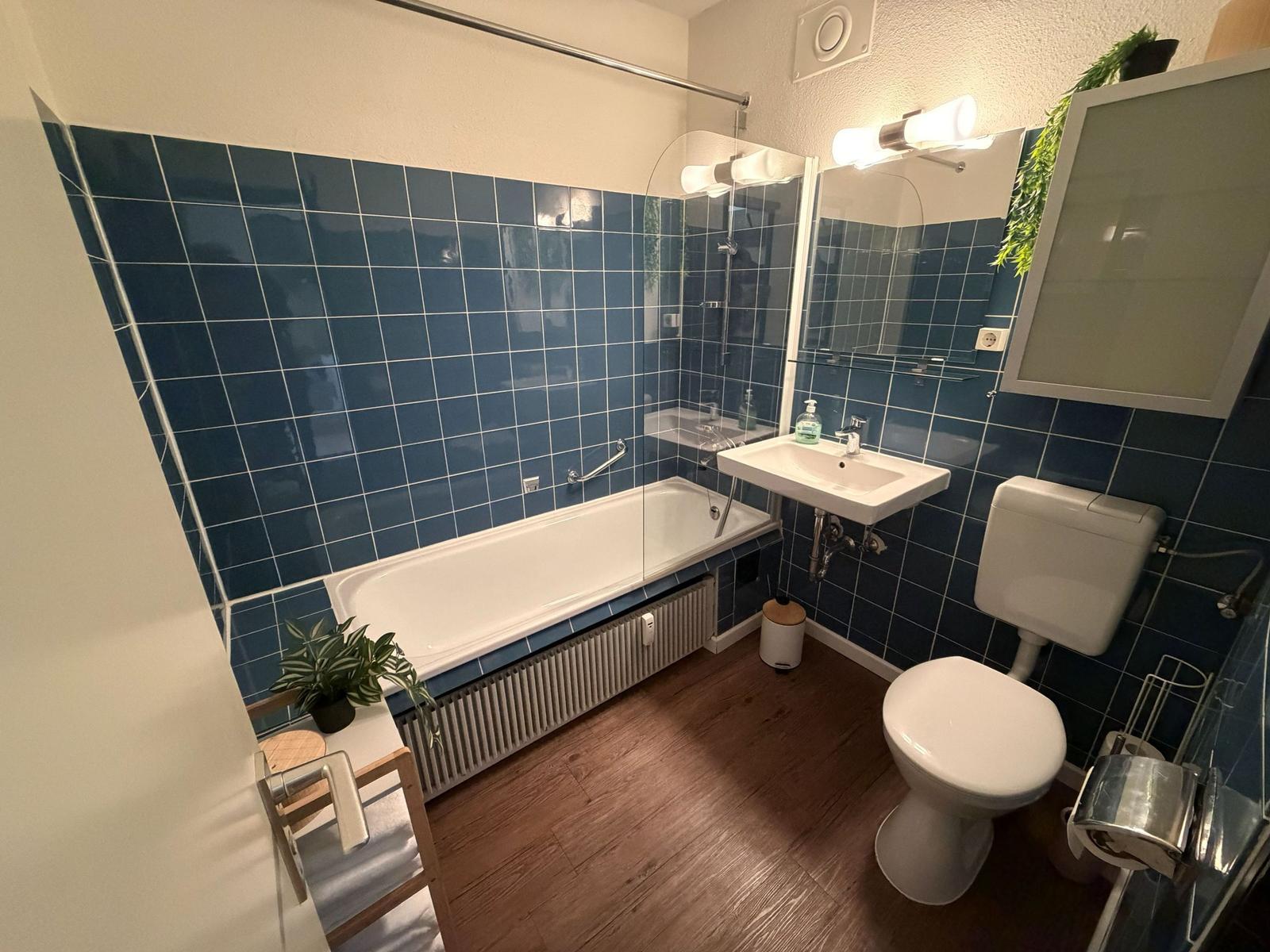 Badezimmer mit Badewanne, Waschbecken und Toilette. Blaue Fliesen an den Wänden.