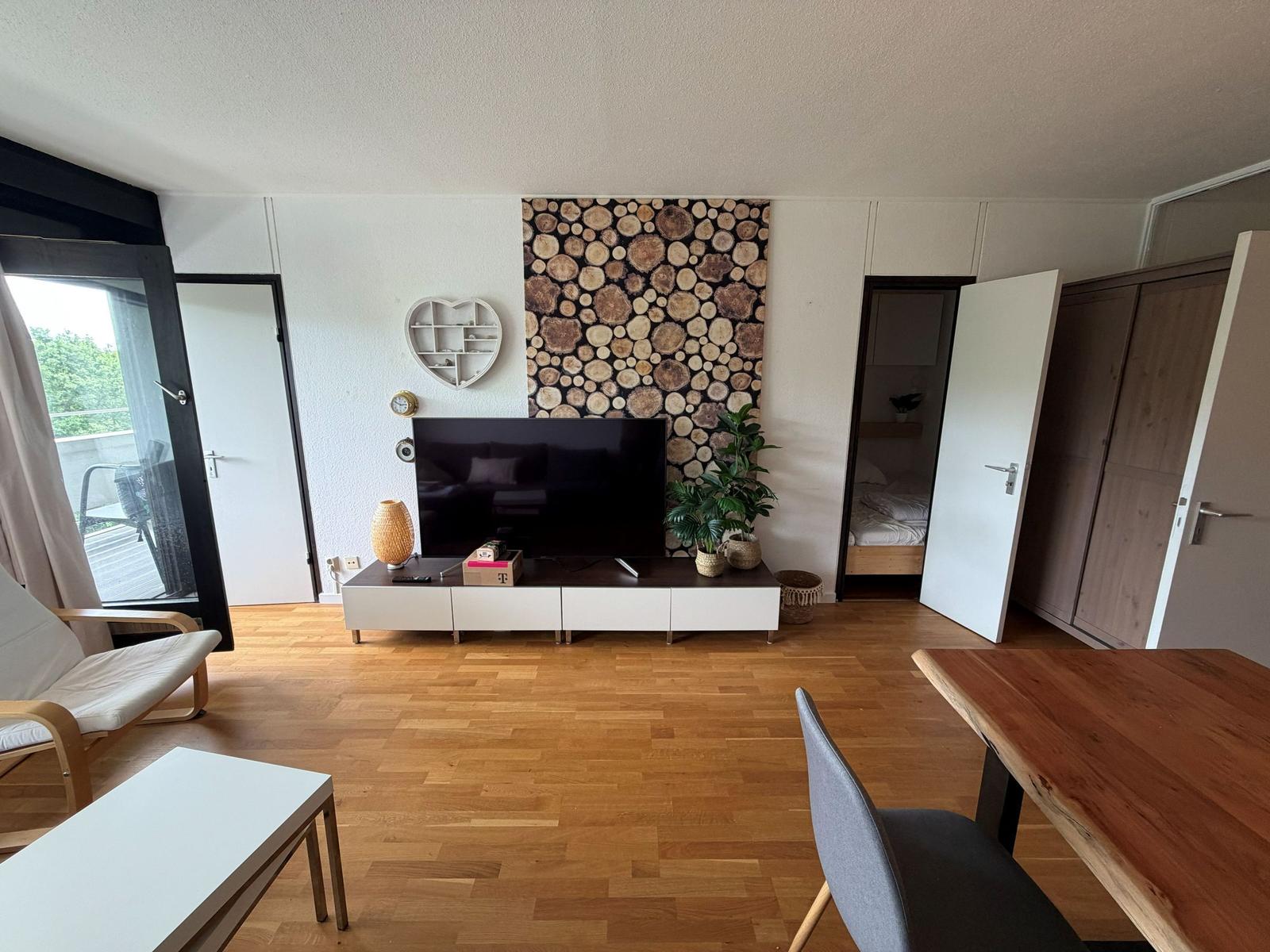 Wohnzimmer mit Holzfußboden, Fernseher und Schlafzimmer im Hintergrund.