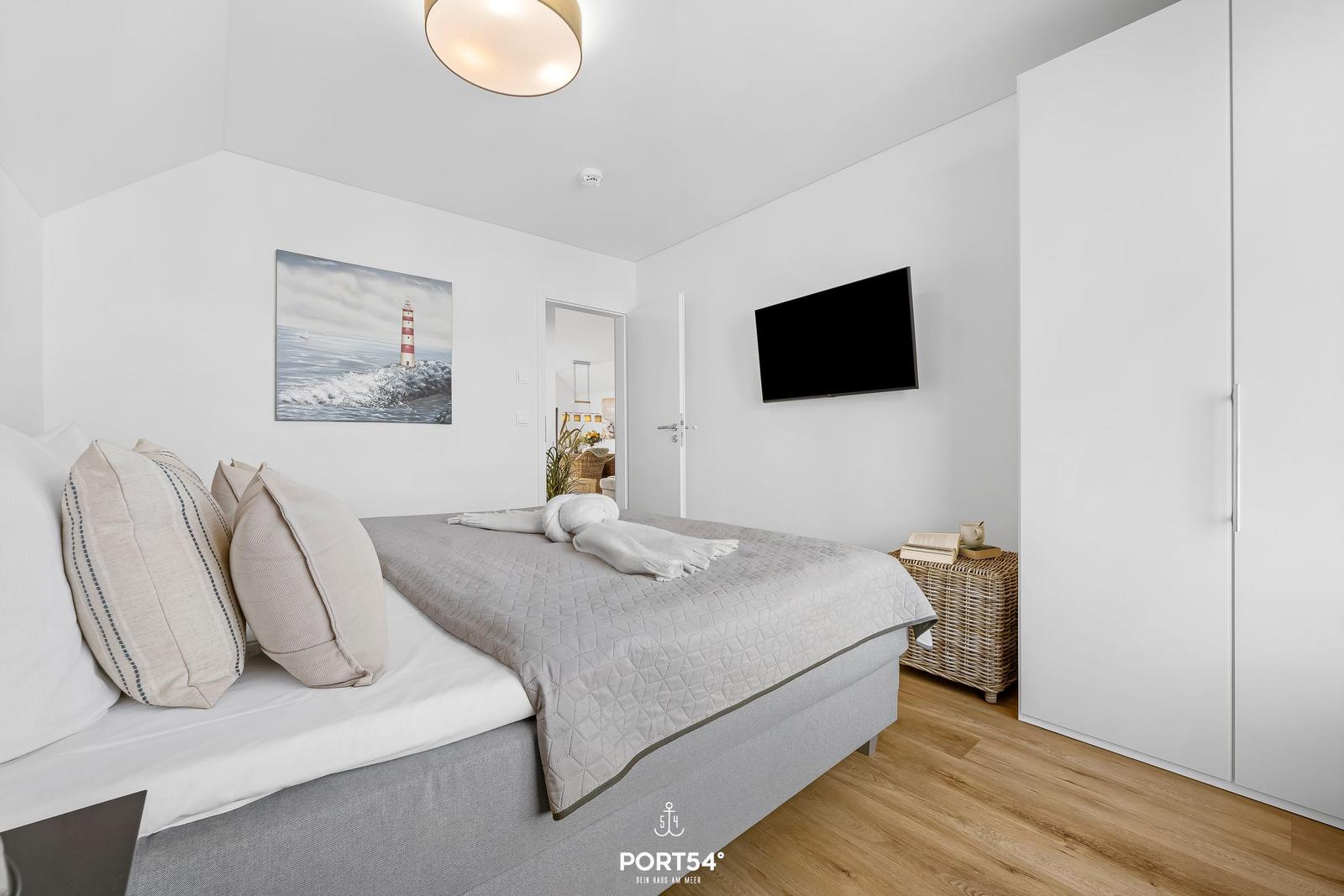 Schlafzimmer mit Bett, Wandbild, Fernseher und Kleiderschrank.
