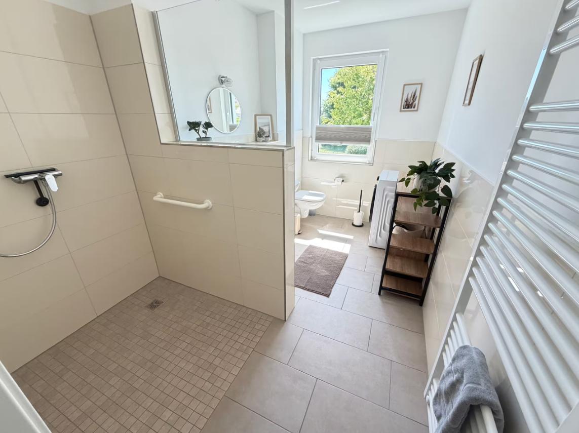 Bad mit Dusche, Toilette und Fenster mit Blick auf Grün.