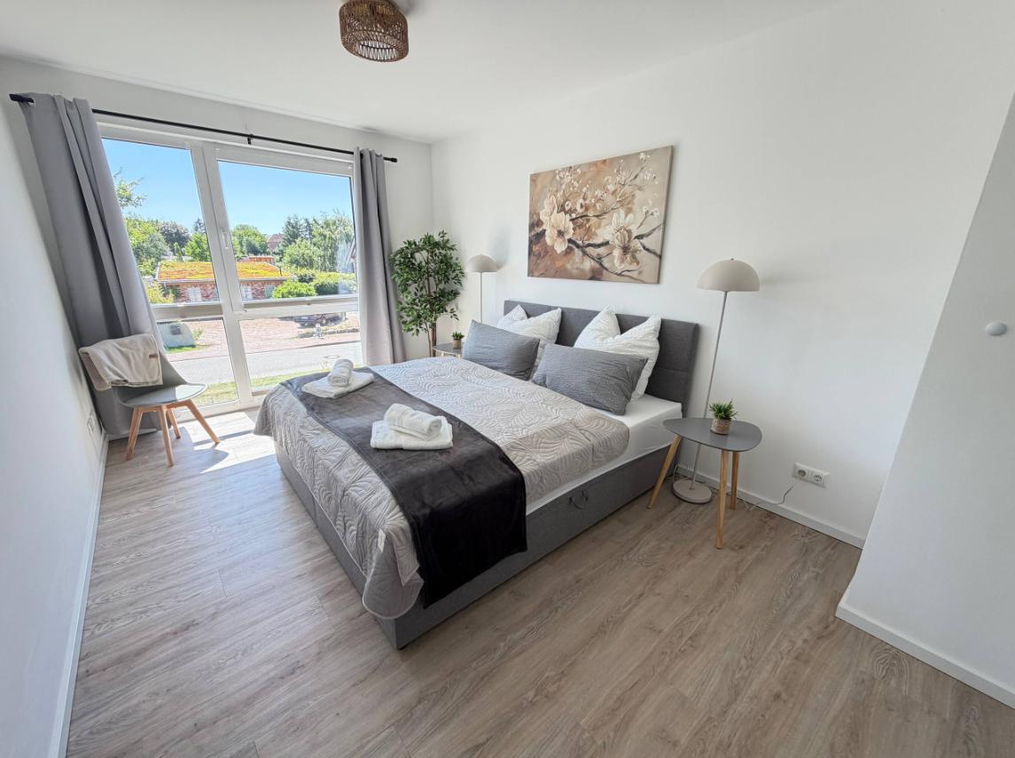 Schlafzimmer mit Doppelbett, Fenster und Wandbild.