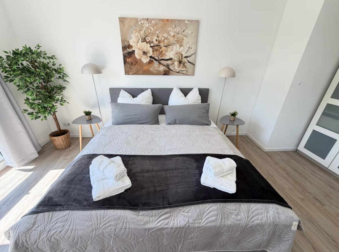 Schlafzimmer mit Bett, Wandbild, Nachttischen und Zimmerpflanze.