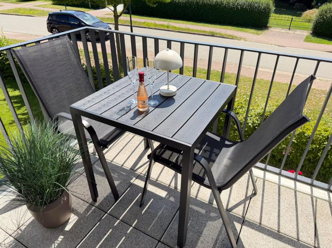 Terrasse mit Tisch, zwei Stühlen, Lampe und Flasche Wein.