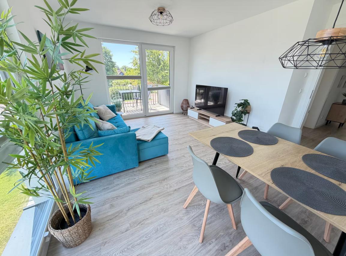 Wohn- und Essbereich mit blauem Sofa, Esstisch und Balkonansicht.