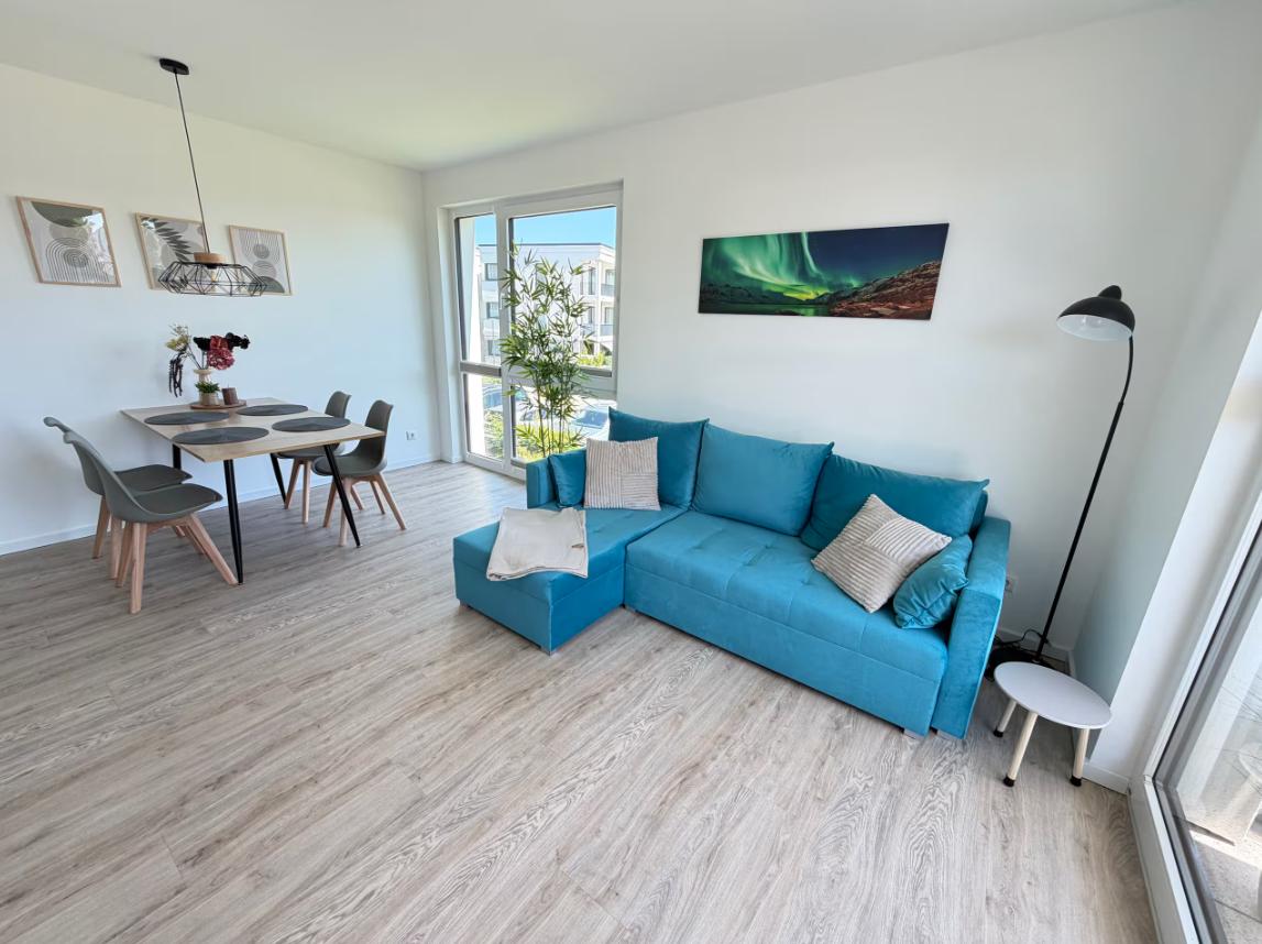 Wohn- und Essbereich mit blauem Sofa, Esstisch und großen Fenstern.