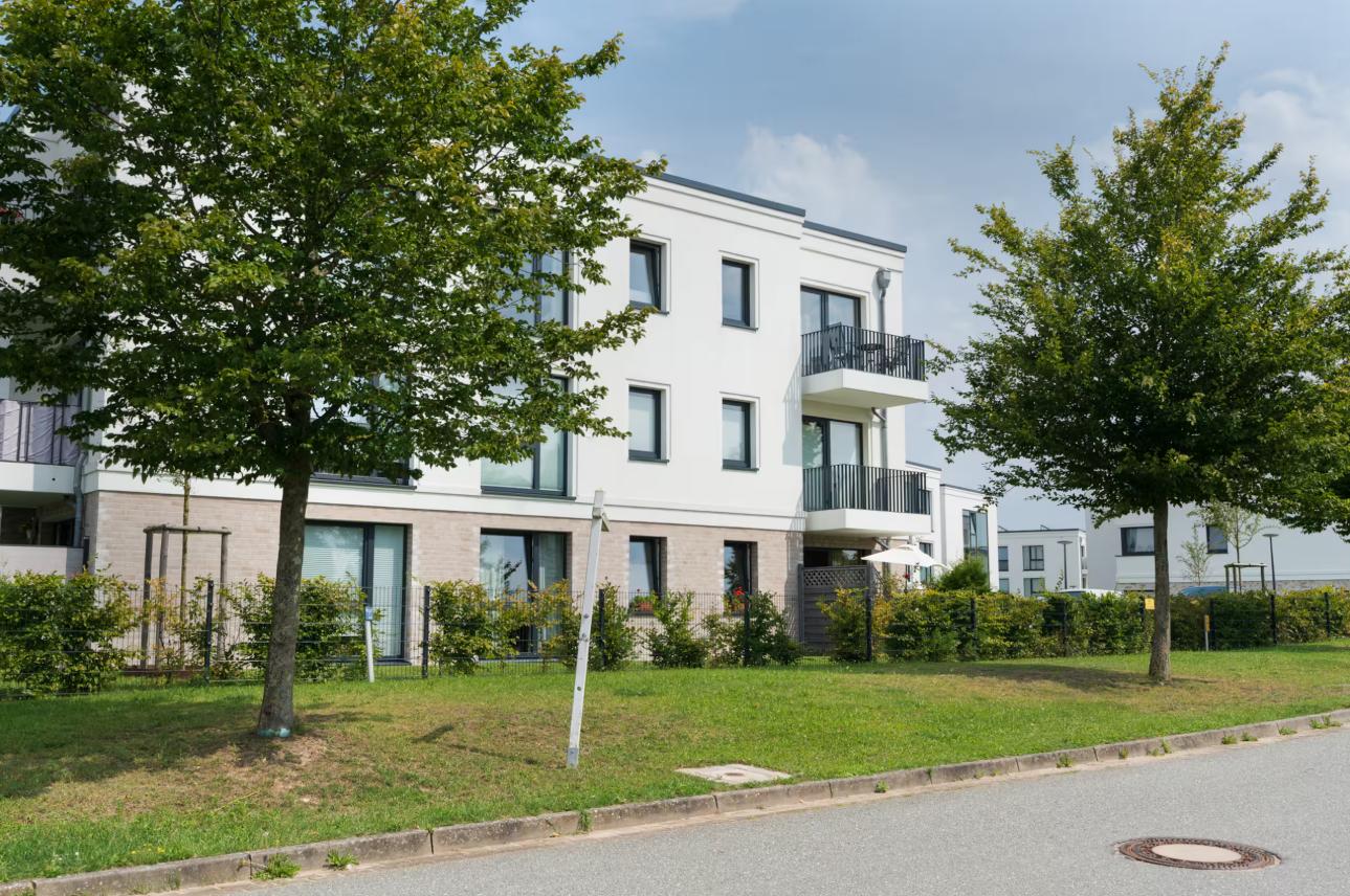 Moderne weiße Wohnhaus mit Balkonen und grünem Gartenbereich.