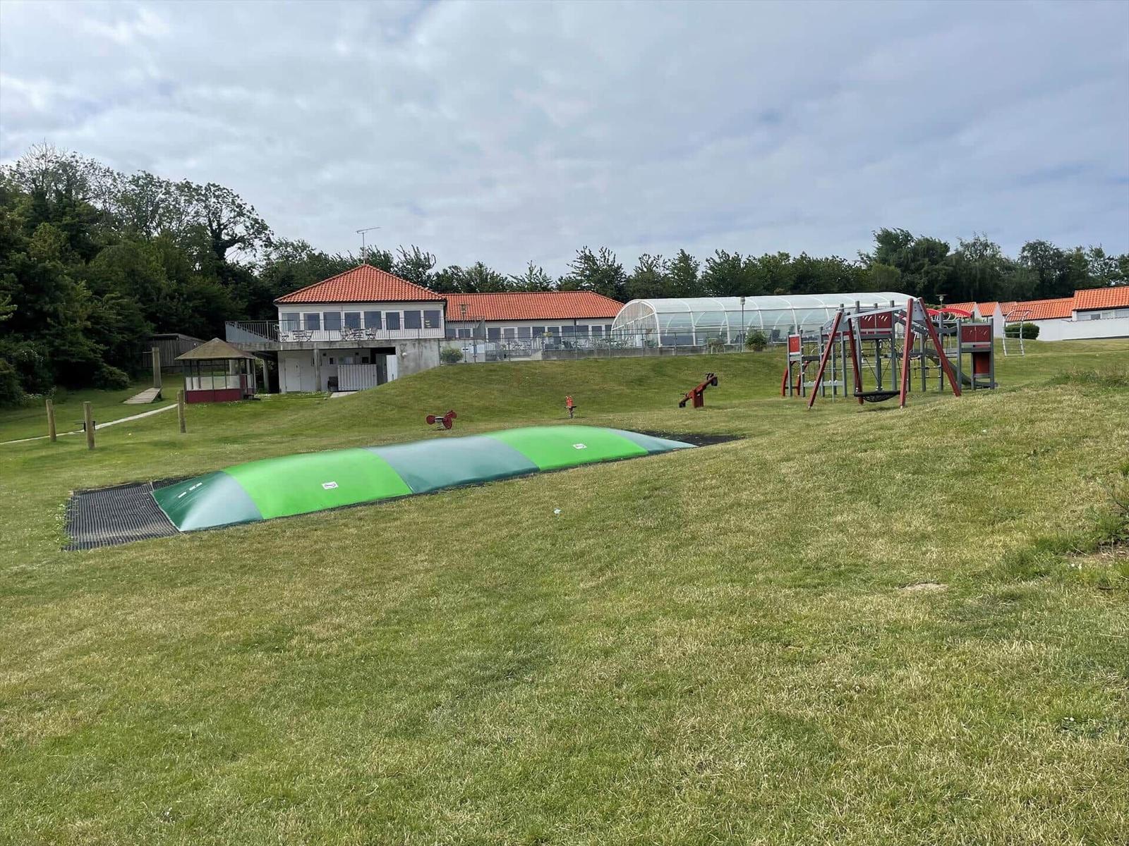 Green playground with slide and climbing frame on grassy area.