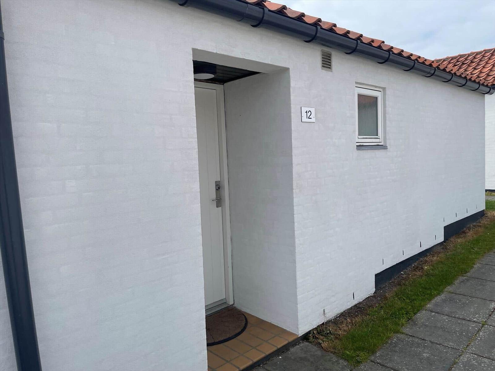 Entrance with door and window on white facade with tiled roof.
