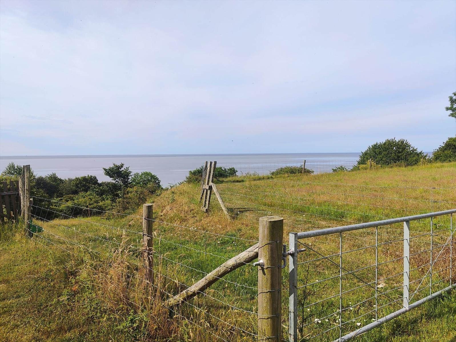 Hinter einem Zaun eröffnet sich ein Blick auf das Meer.