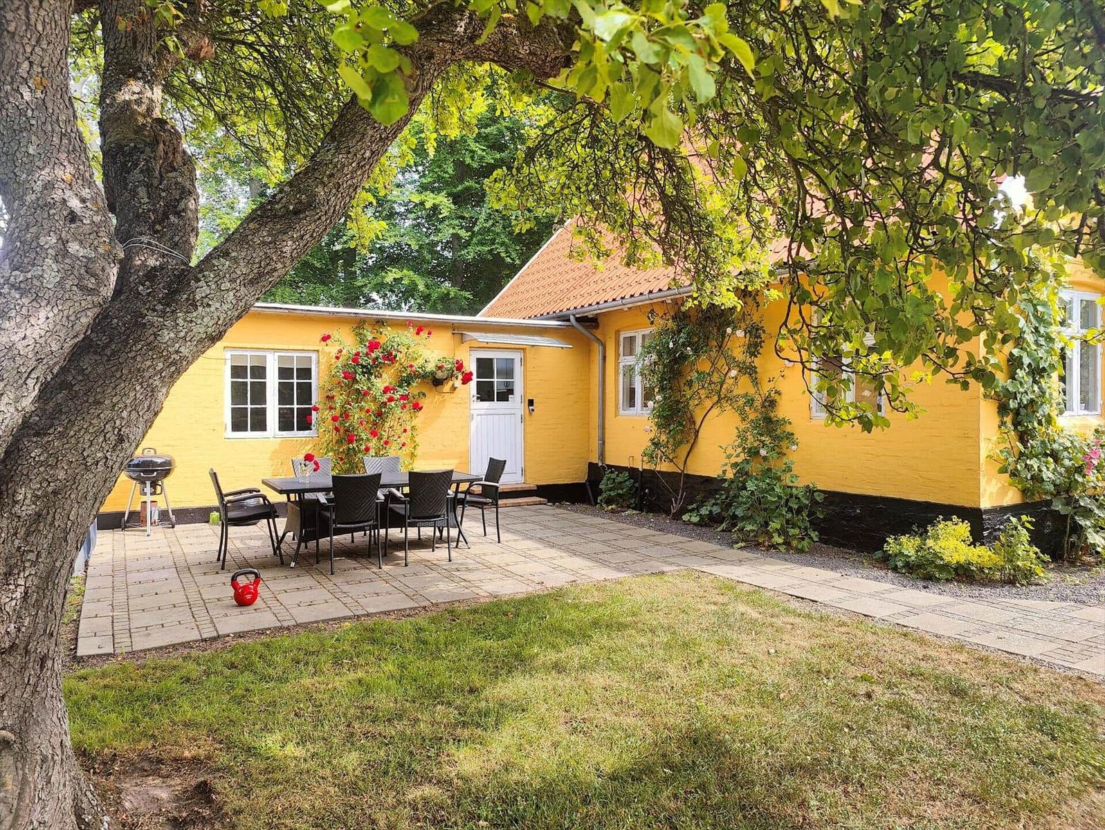 Gelbes Haus mit Terrasse, Grill und Garten. Rote Rosen an der Wand.