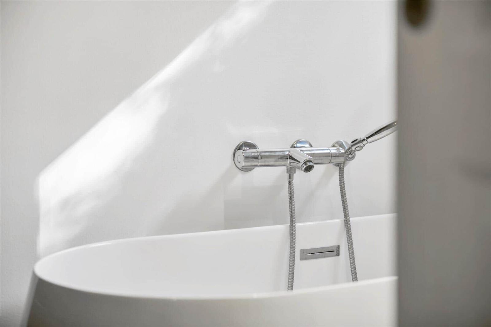 Eine weiße Badewanne mit chromfarbenem Wasserhahn und Duschbrause.