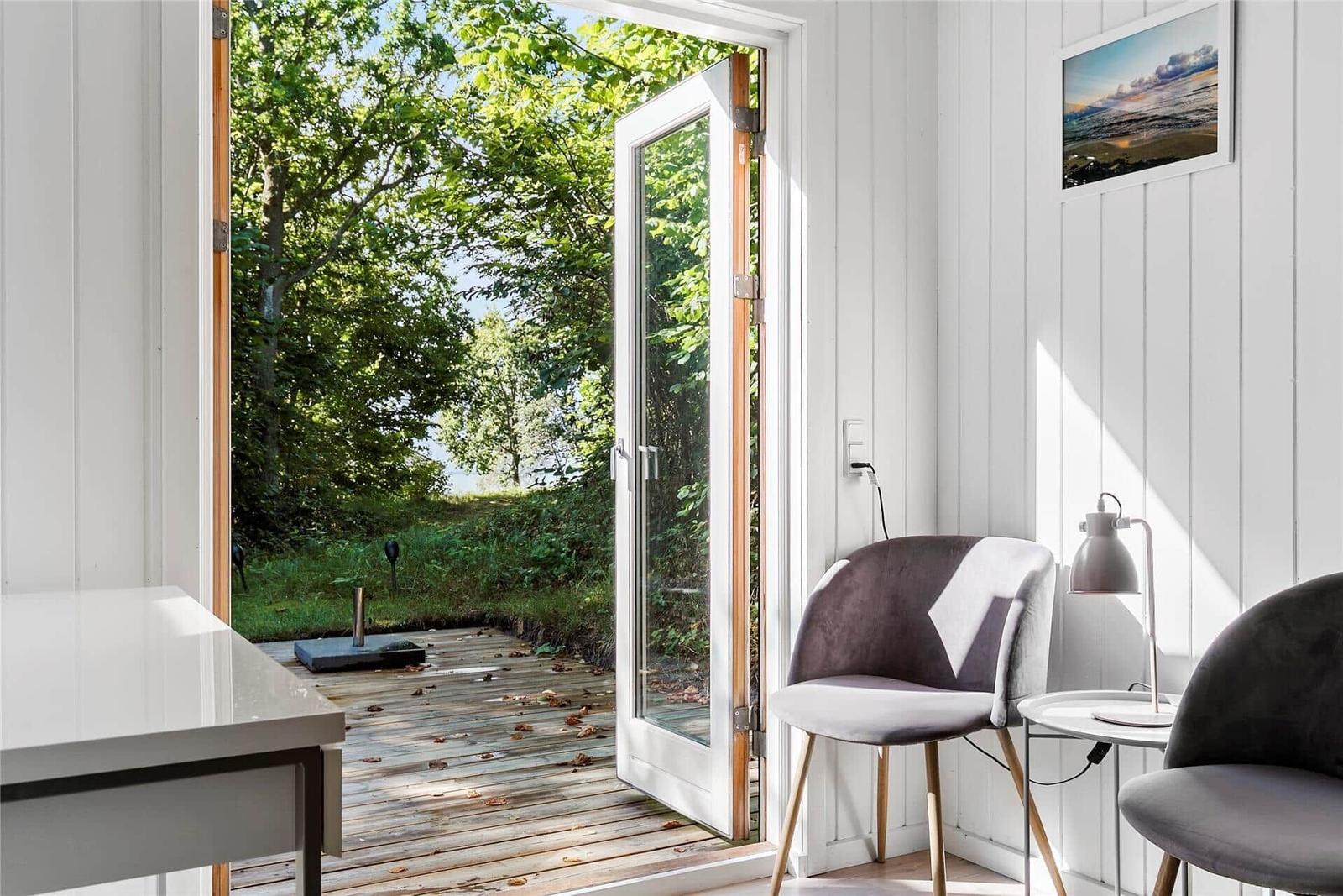 Durch die Glastür blickt man auf eine Holzterrasse und grüne Bäume.