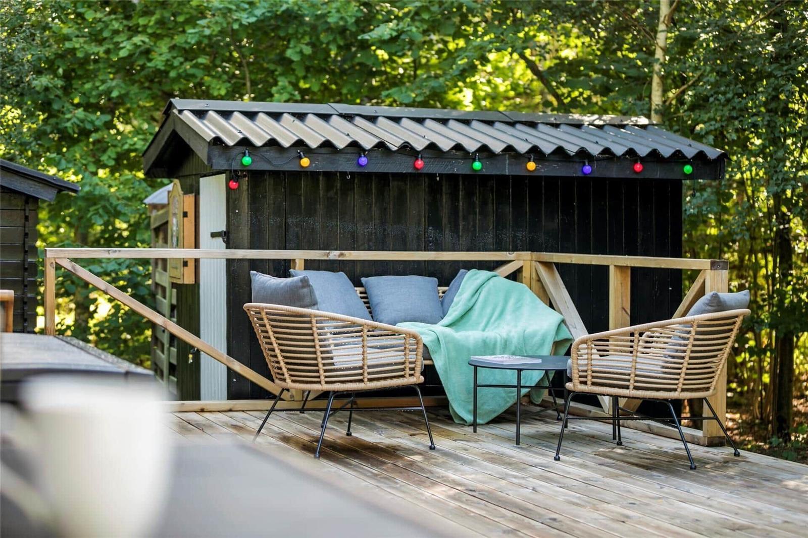 Terrasse mit Sitzgelegenheit vor einem Holzschuppen mit bunten Lichterketten.