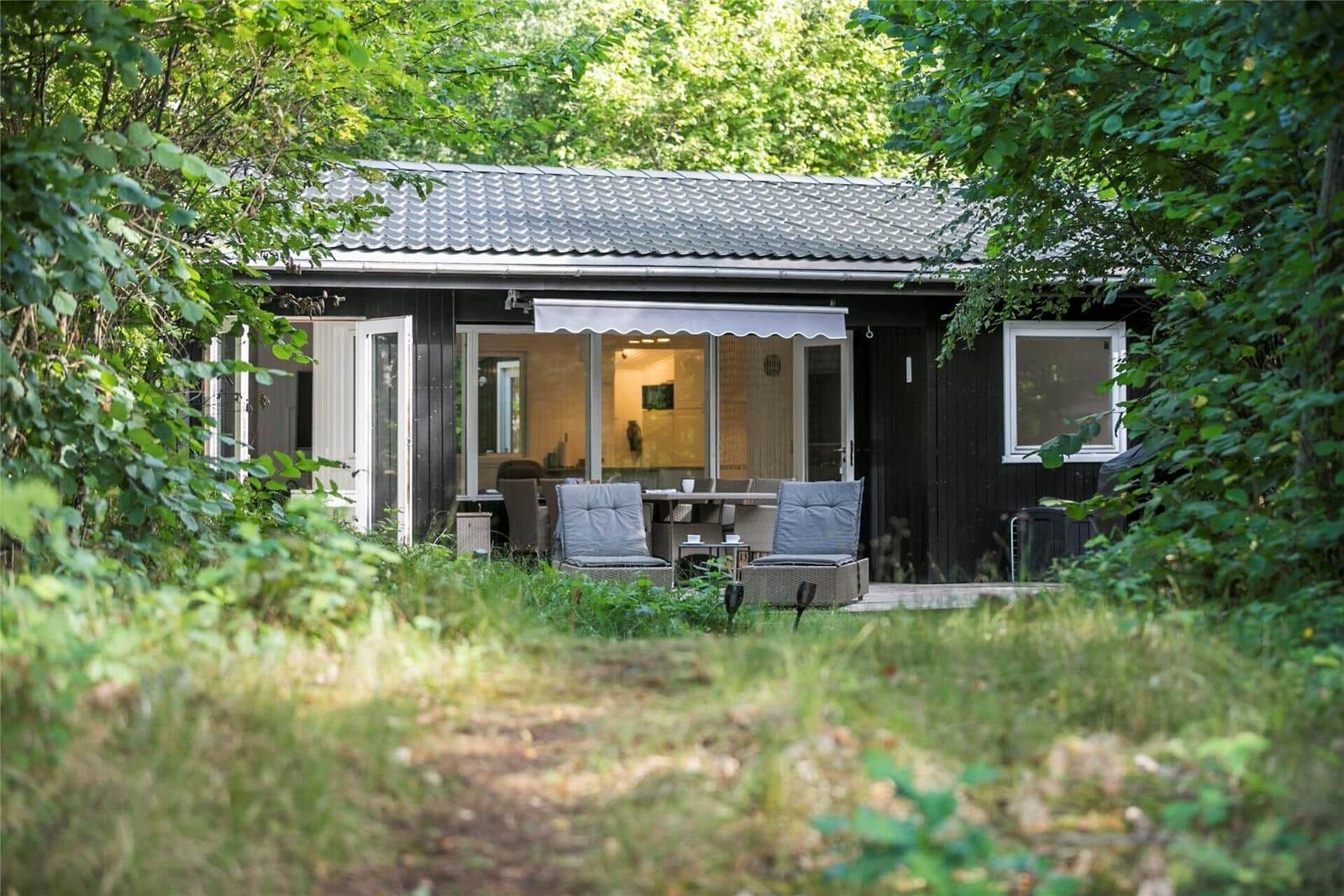 Ein Holzhaus mit Terrasse und Sitzgelegenheiten im Grünen.
