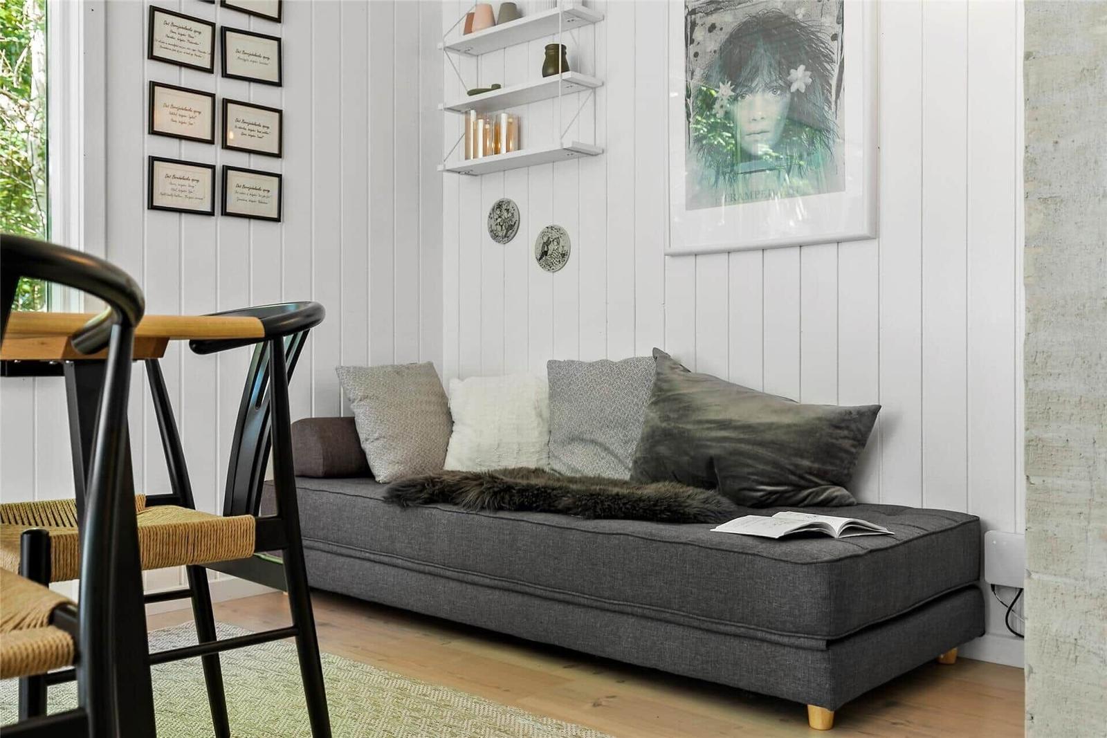 Ein grauer Sofa mit Kissen und Fell liegt in einem Raum mit weißen Wänden und einem Stuhl.