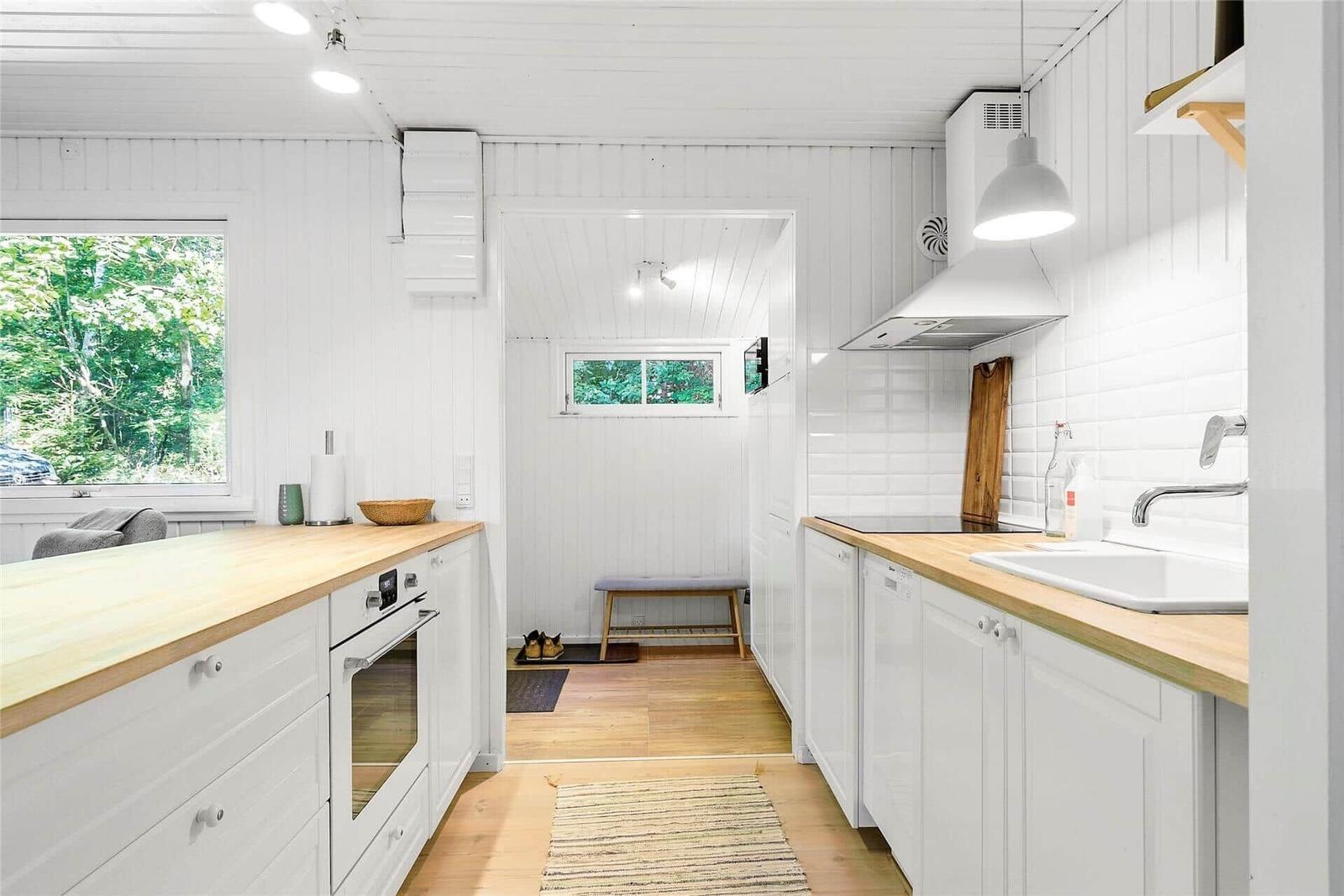 Küche mit Holz Arbeitsfläche, weißen Schränken und Fenster zum Wald.